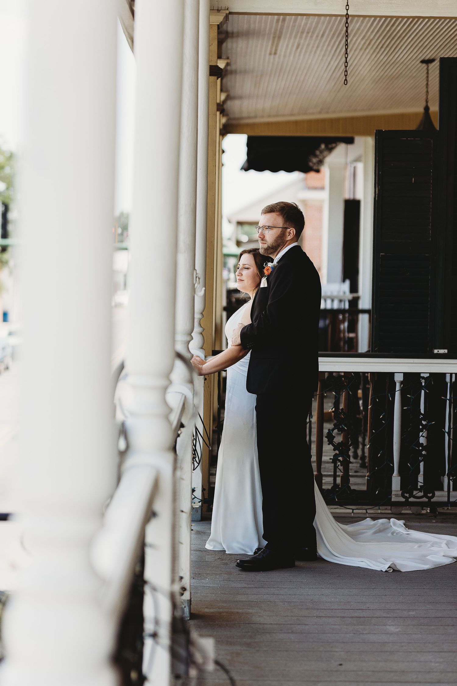 Wedding couple sharing intimate moment on white columned porch.