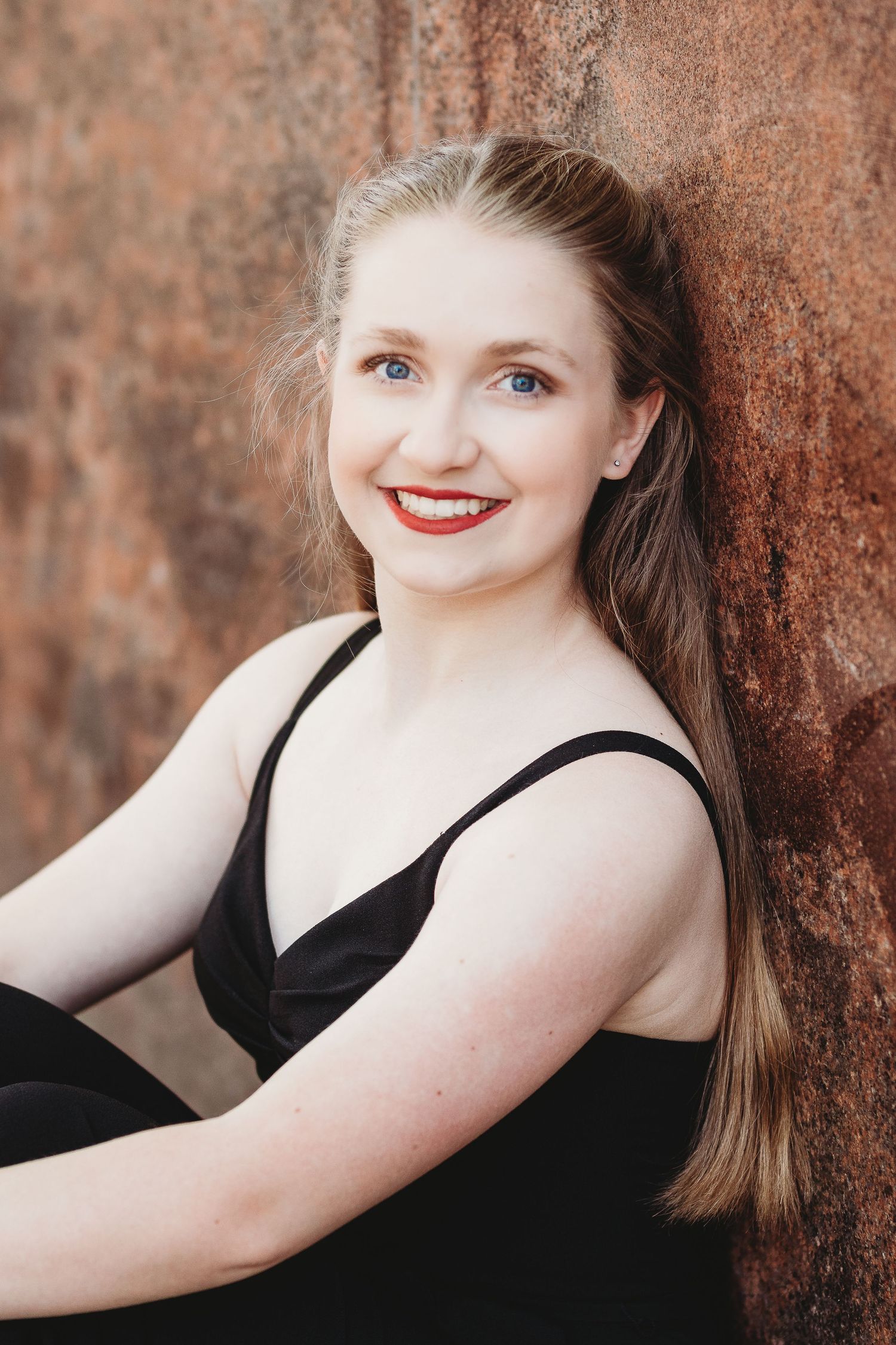 A portrait against a rustic wall wearing a black dress with long hair.