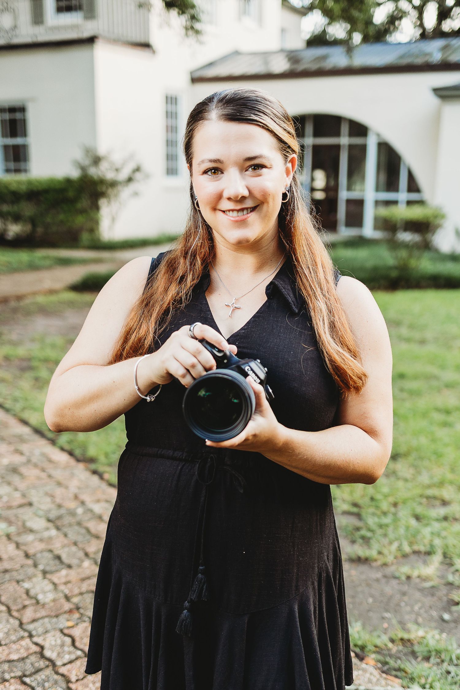 Female photographer in black dress demonstrating camera techniques outdoors.