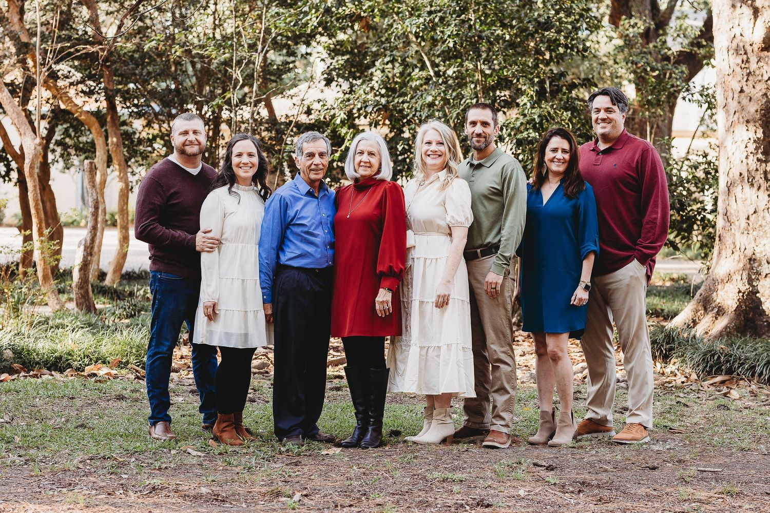 Large extended family gathering outdoors for group photo among trees.