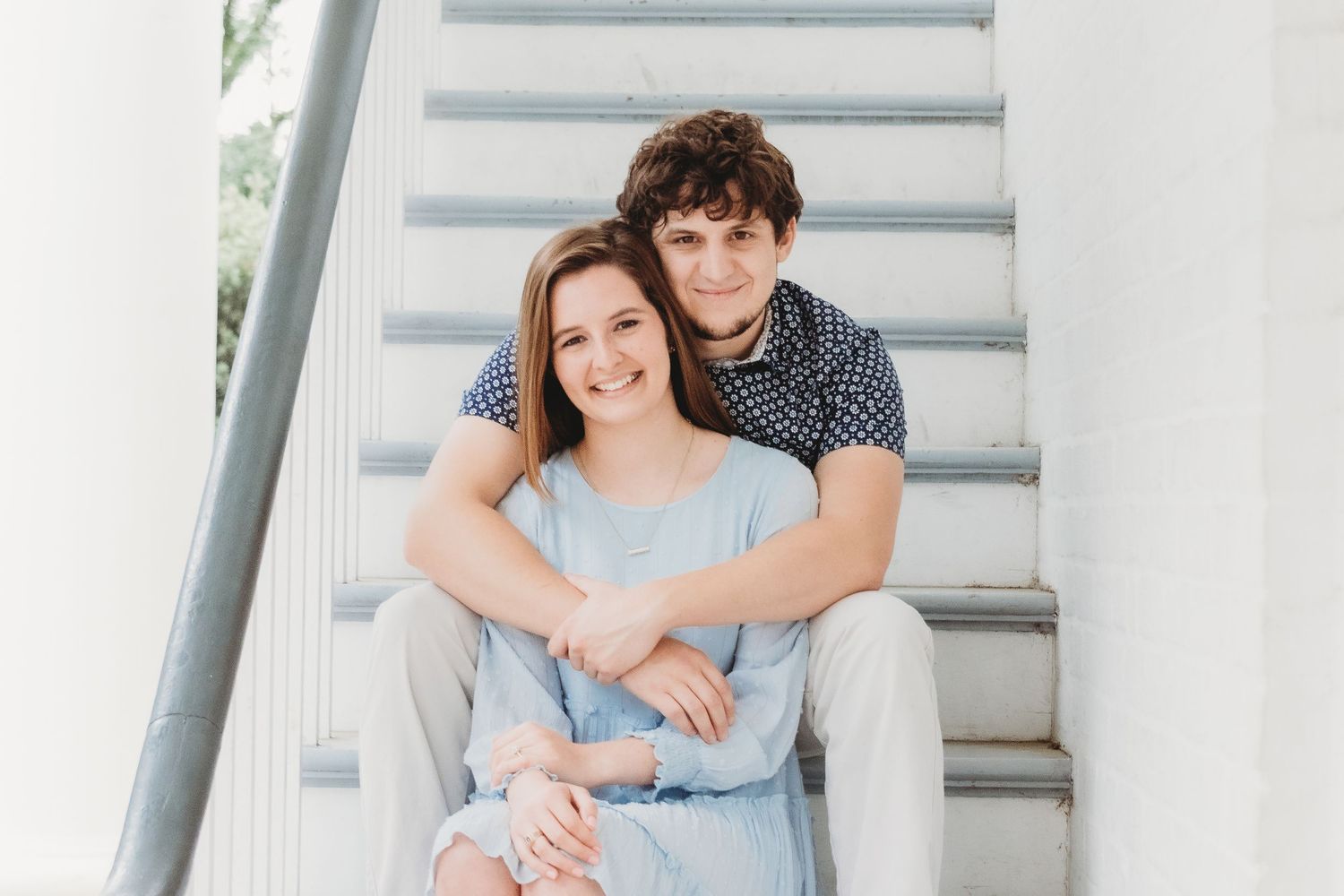 A couple poses on white stairs in casual summer attire.