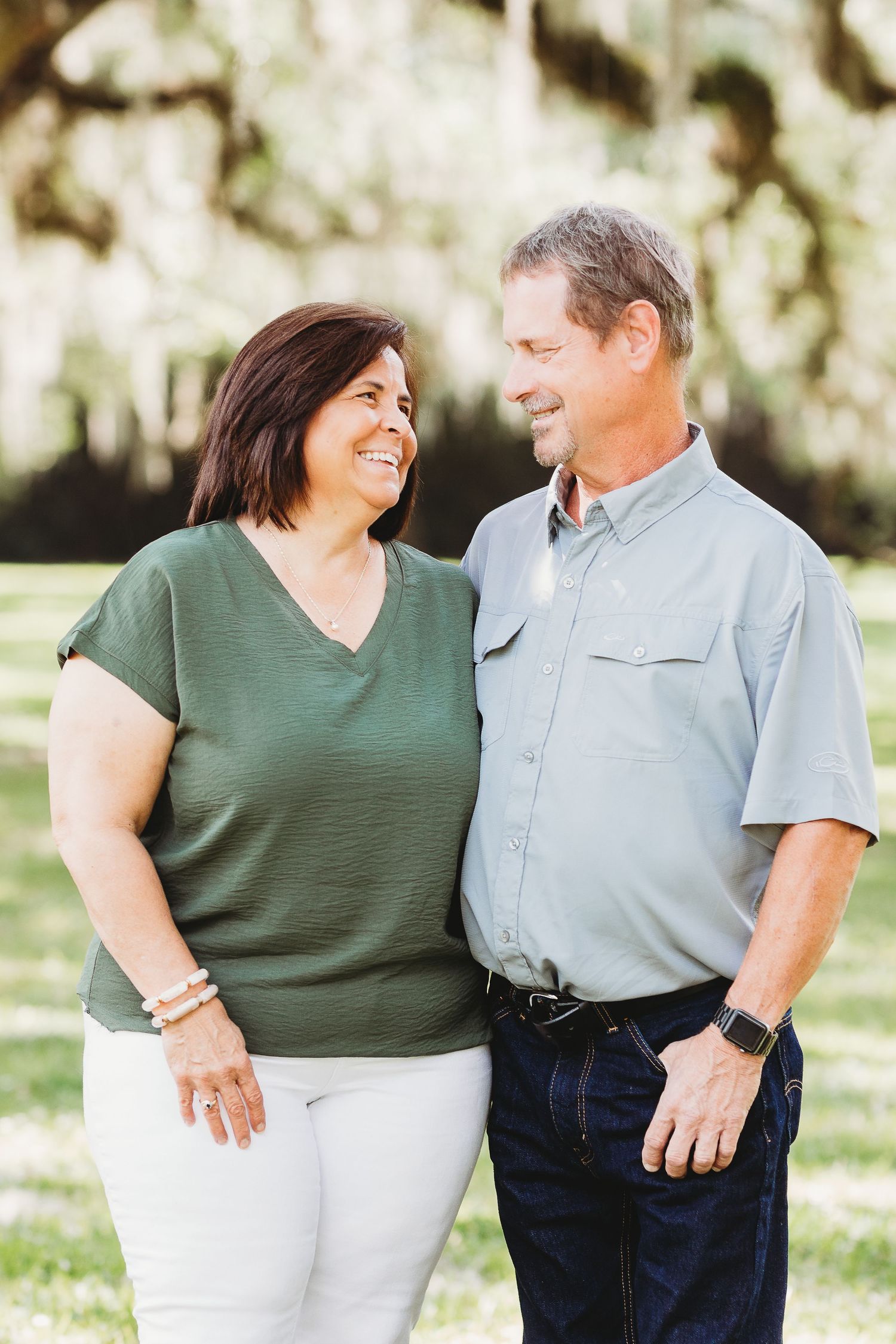 A couple shares a loving moment outdoors under moss-draped trees.