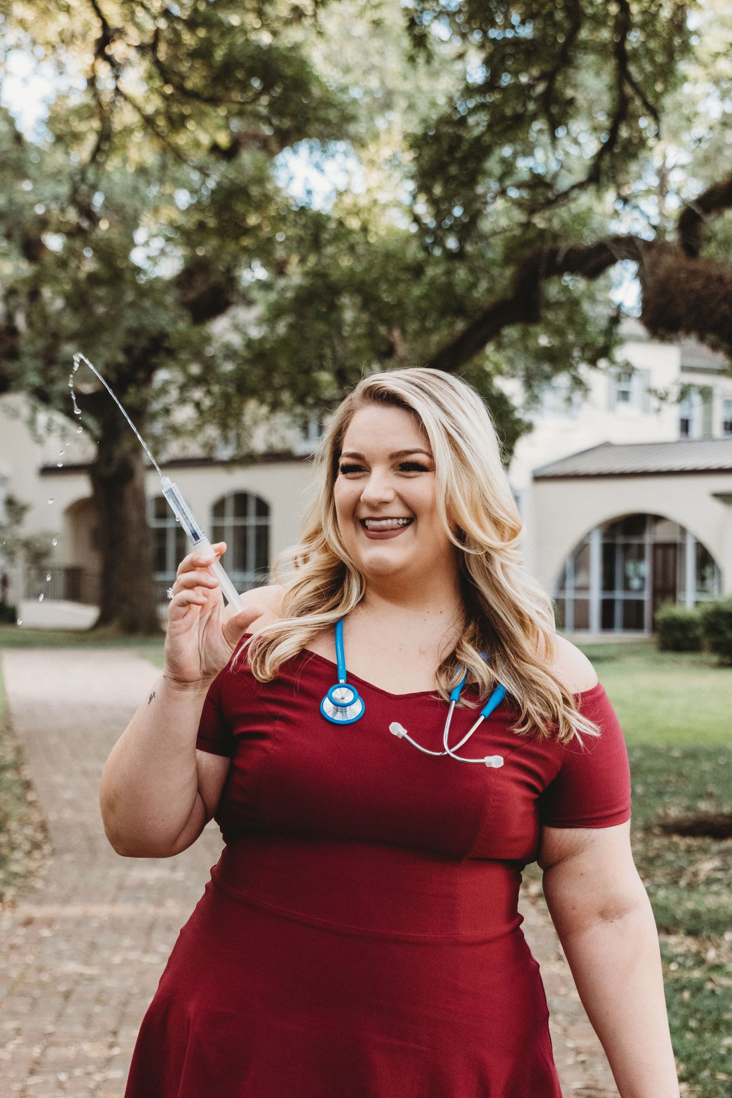 Healthcare professional in burgundy scrubs showing stethoscope outdoors.