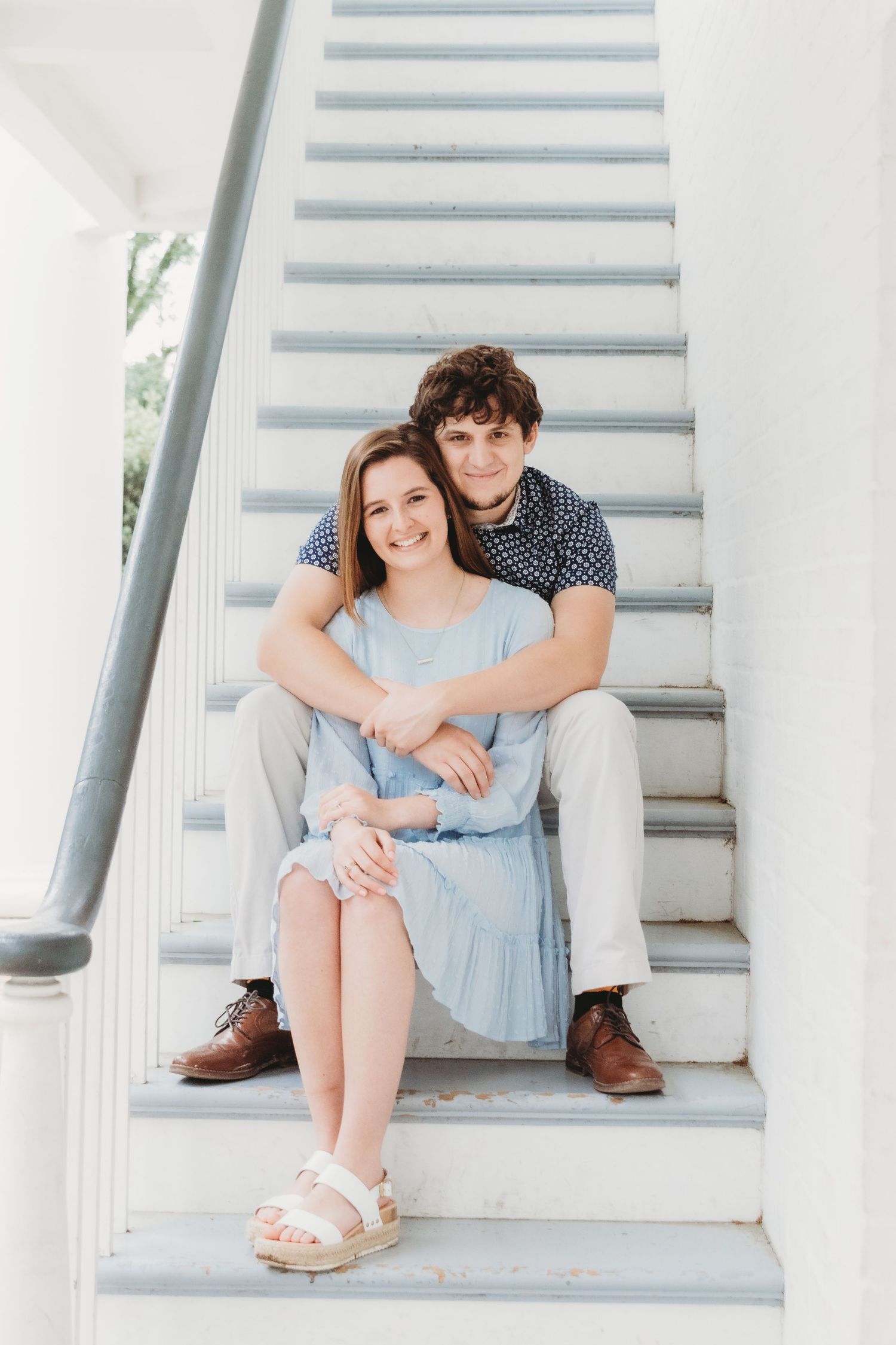 A couple sits together on white stairs sharing an intimate moment.