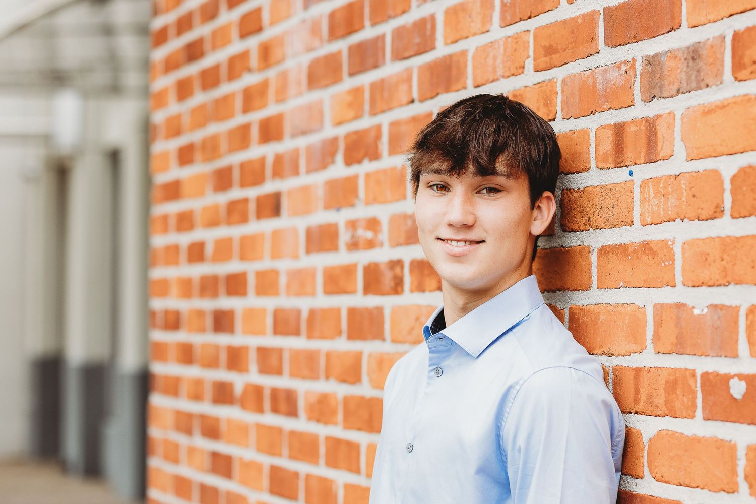 Person in light blue shirt posing against rustic brick wall background.