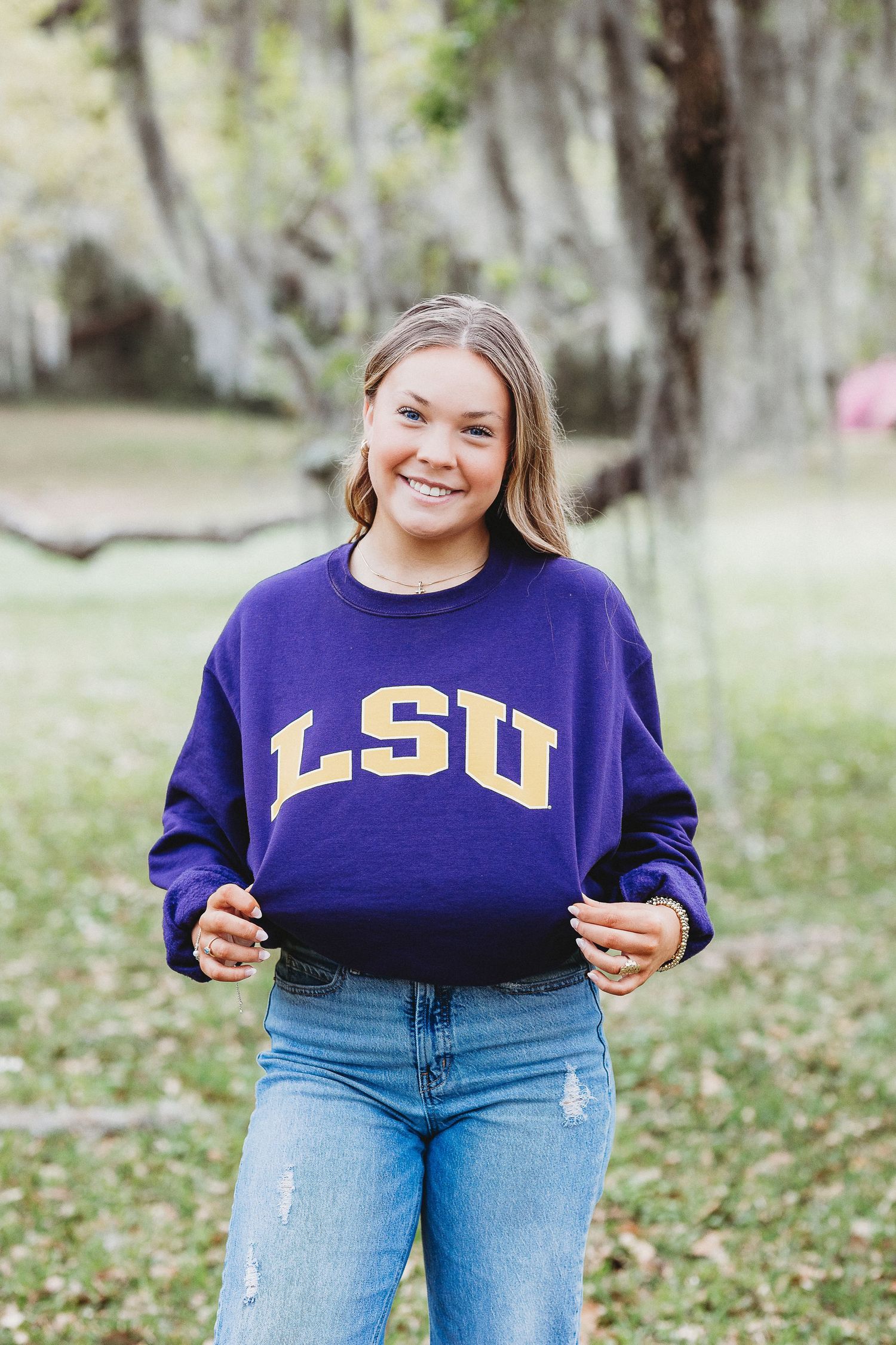 Person in LSU sweatshirt and jeans poses against natural outdoor background.