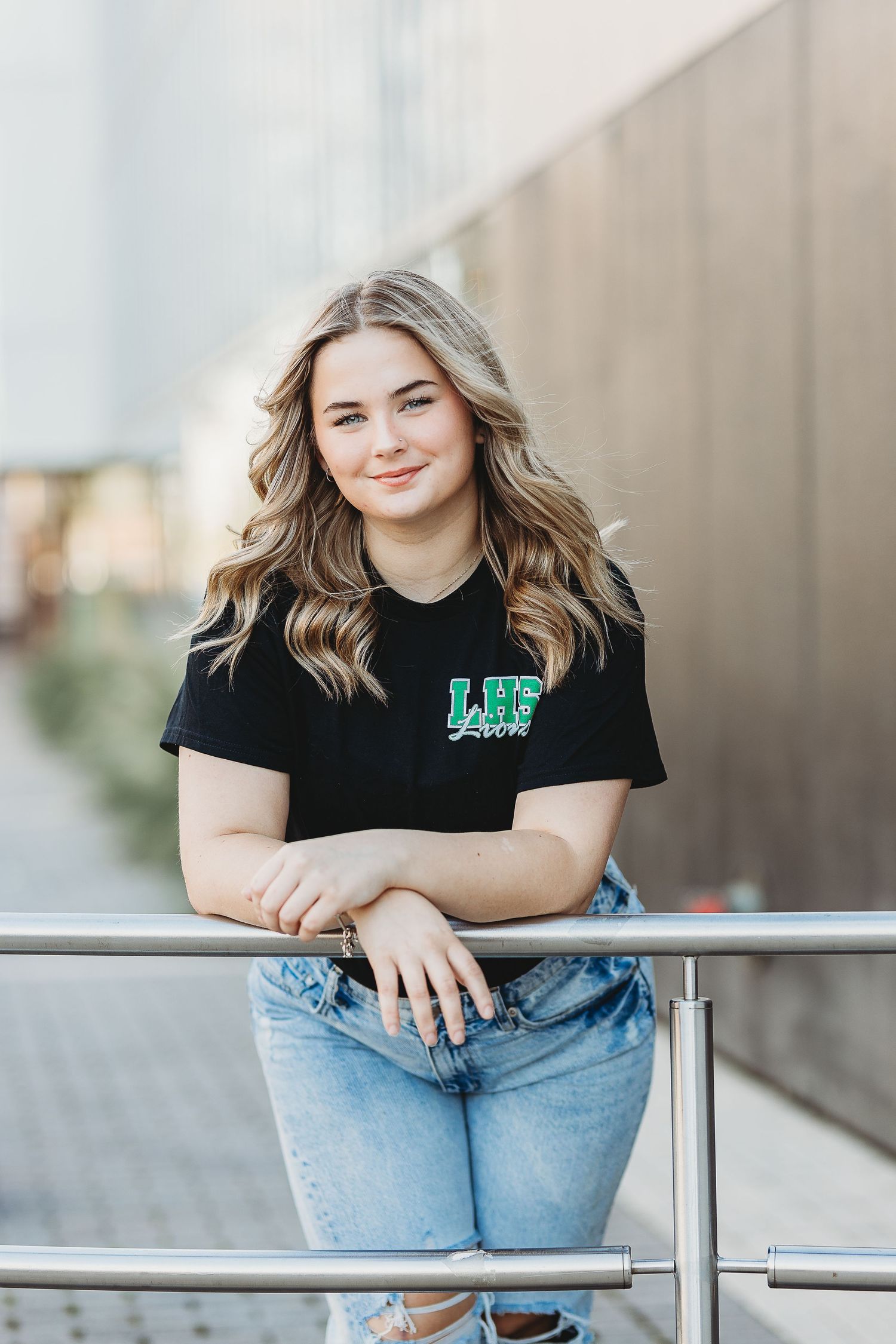 Casual outdoor portrait wearing black t-shirt and jeans while leaning against metal railing.