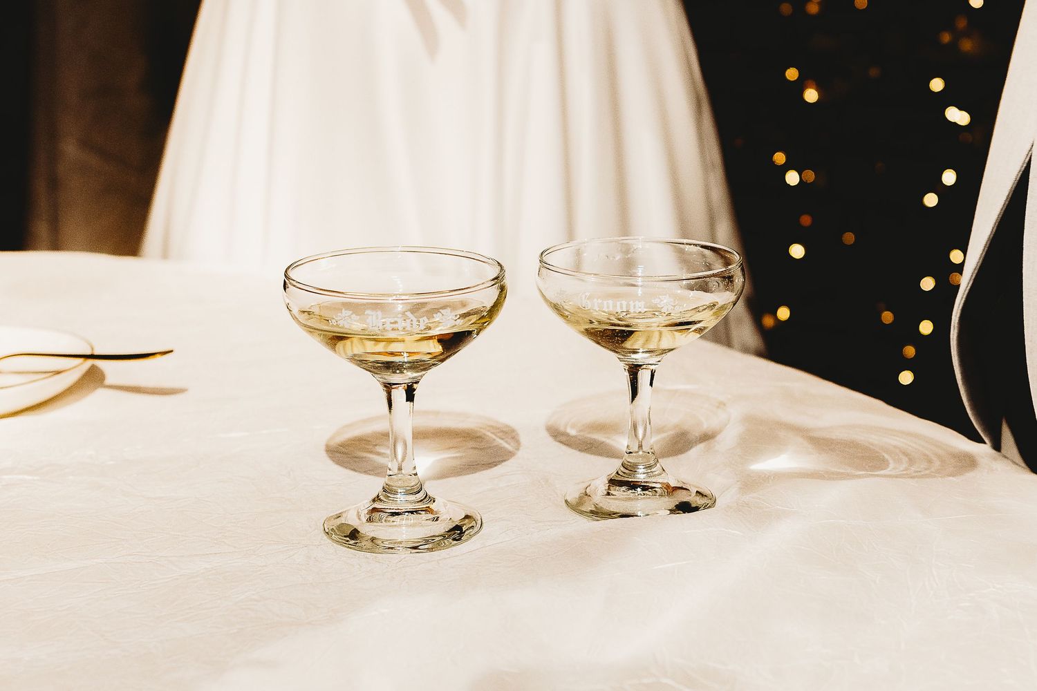 Empty wine glasses on a white tablecloth with twinkling lights in the background.