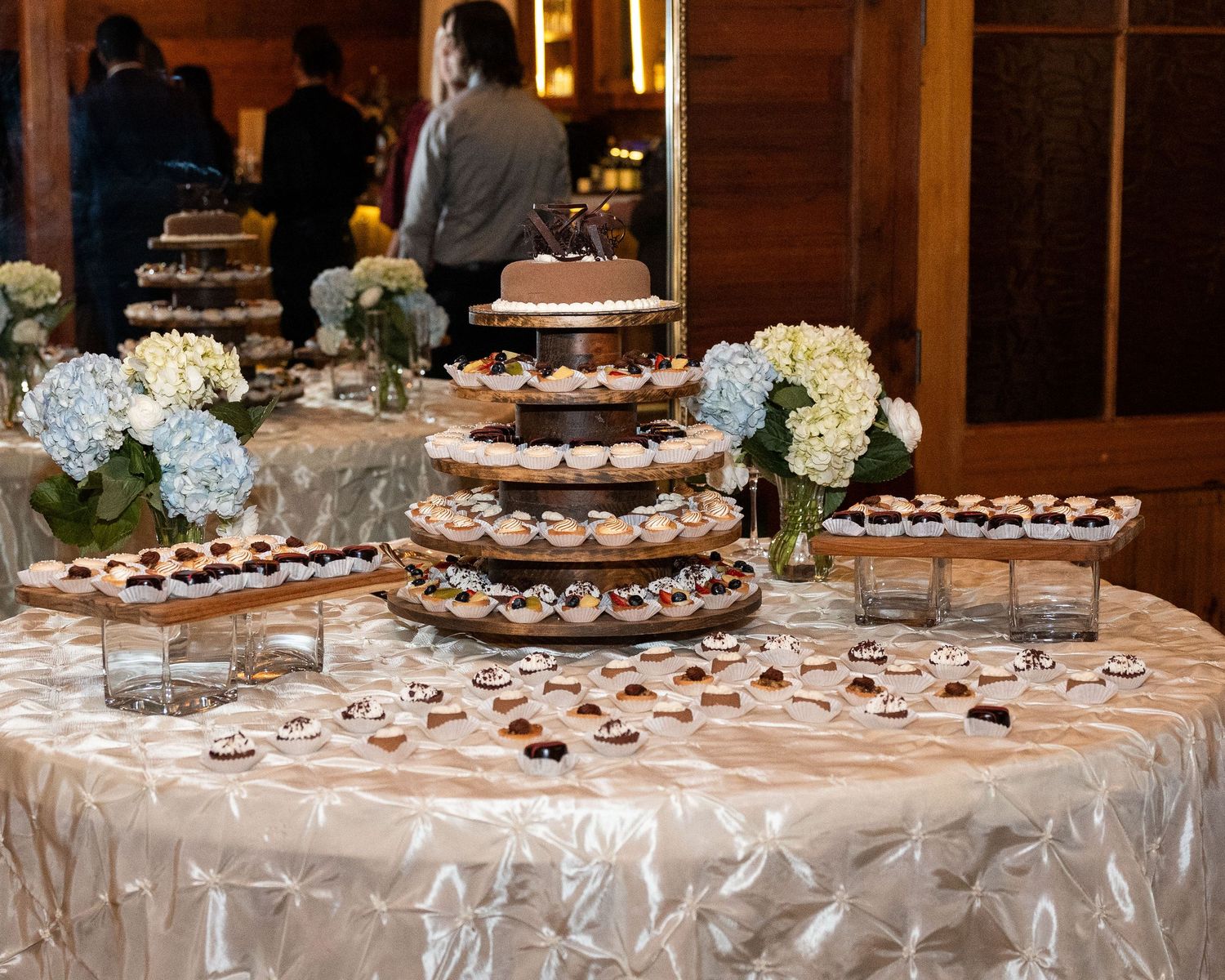 Wedding dessert table with chocolate treats and hydrangea centerpieces displayed on white linens at reception.