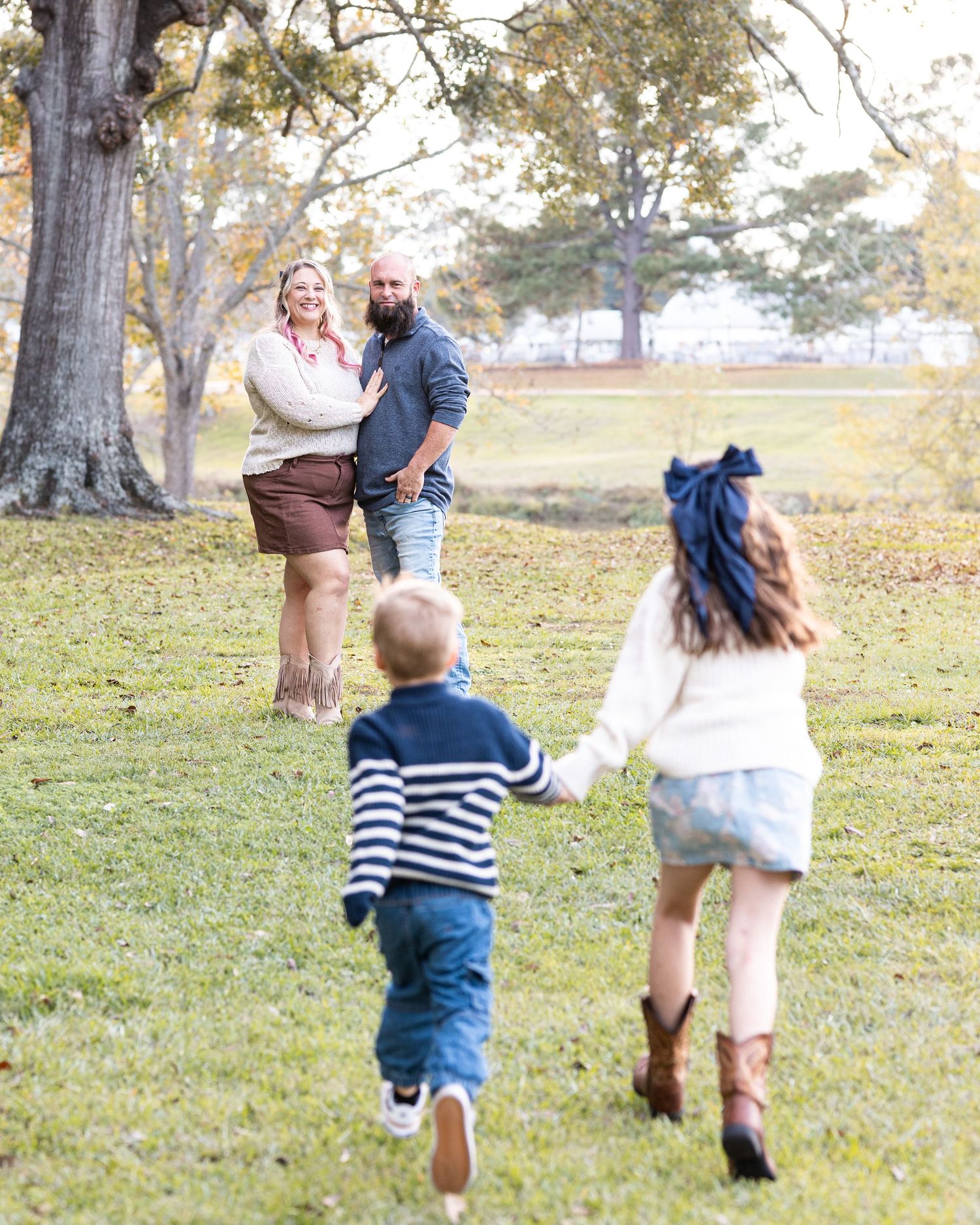 Family walking together on grass with fallen leaves in a park during autumn.