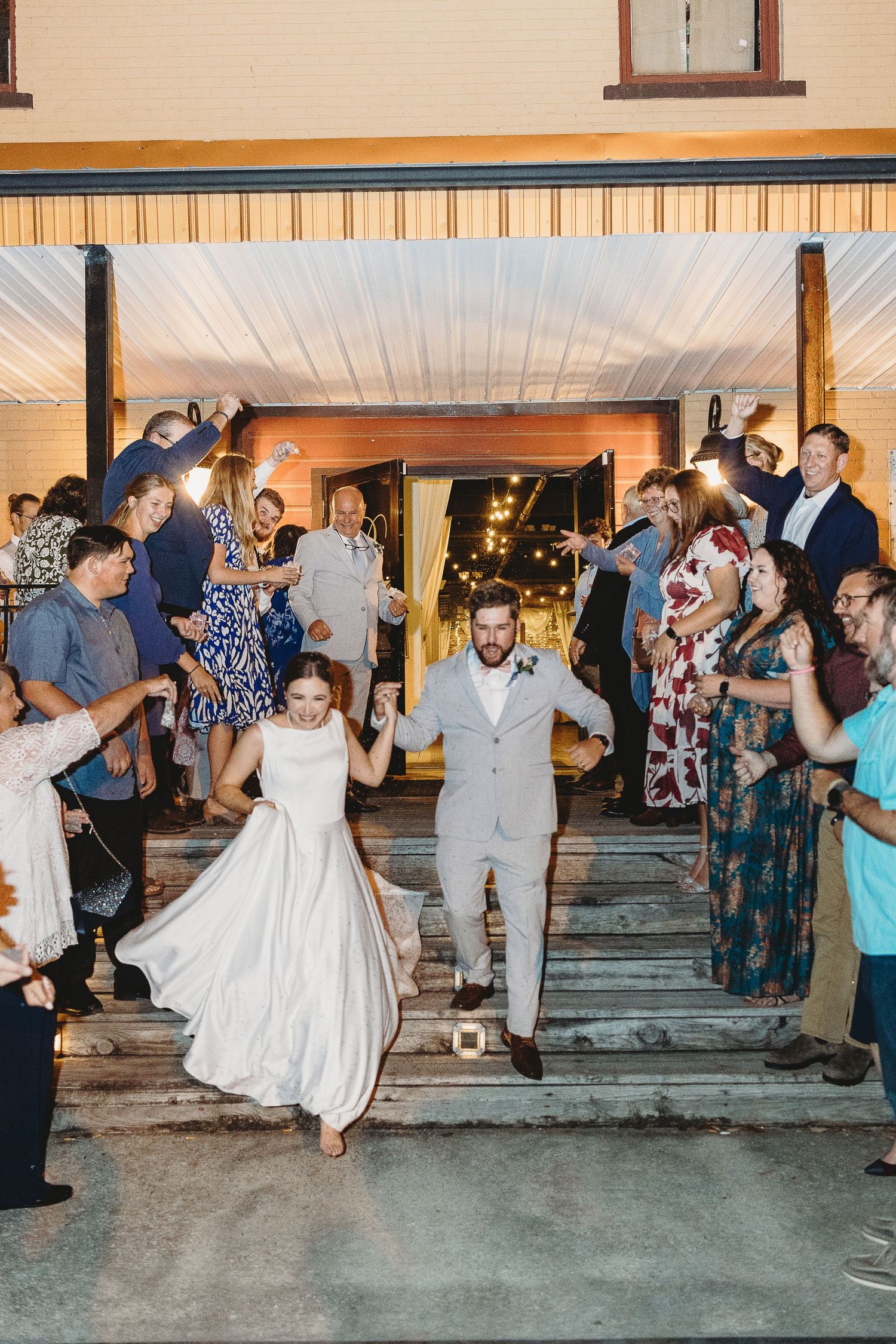 Wedding party dancing outside at dusk with guests cheering and celebrating.