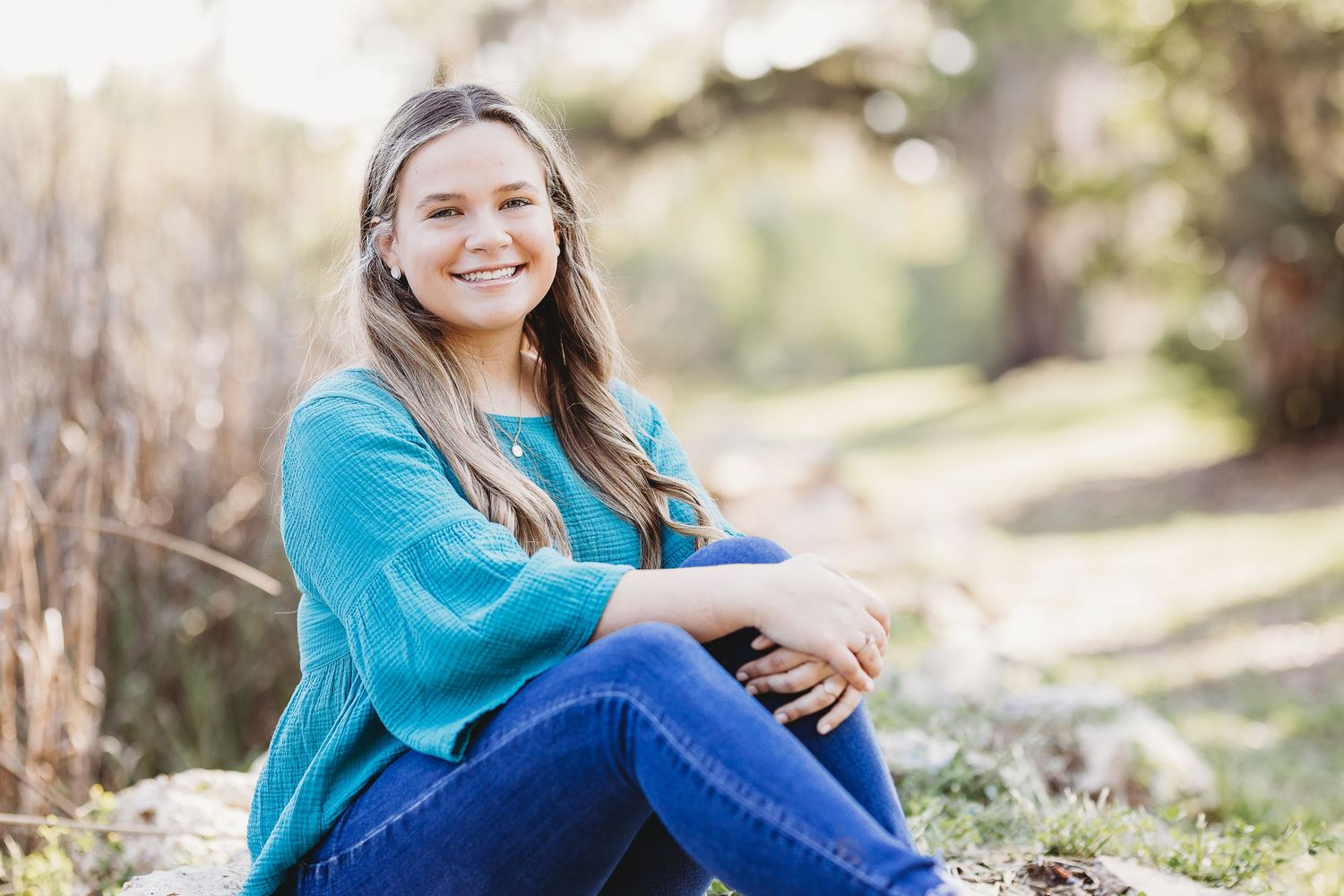 Person in bright blue sweater sits on rocky ground during outdoor portrait session.