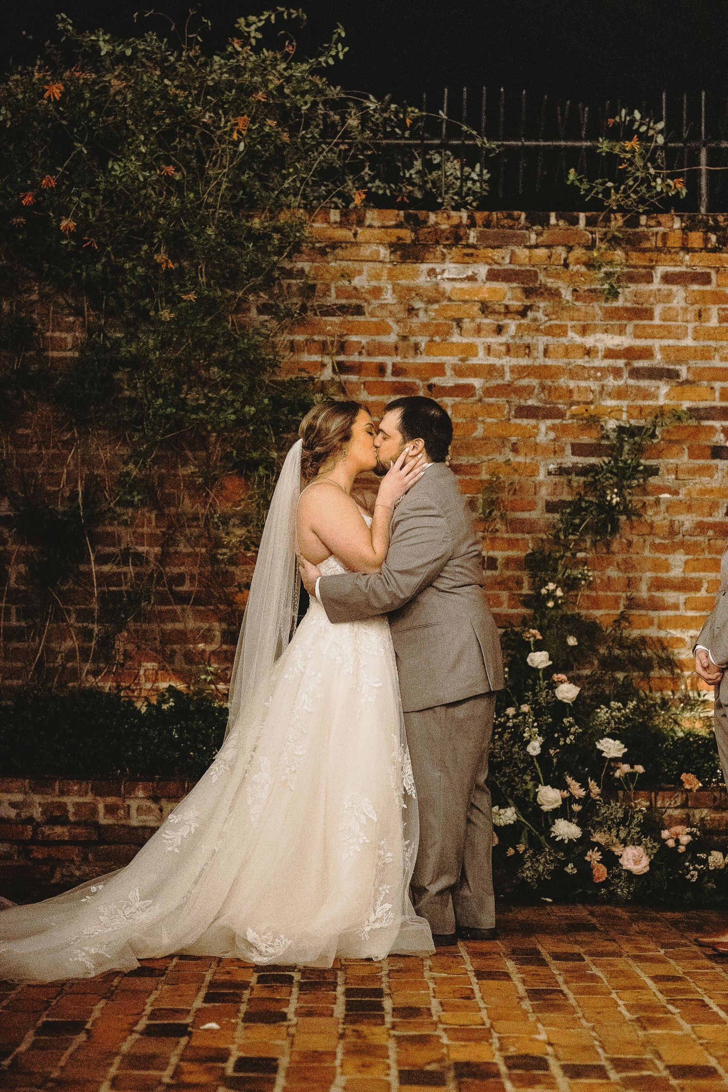 Romantic kiss between newlyweds against rustic brick wall with climbing roses.