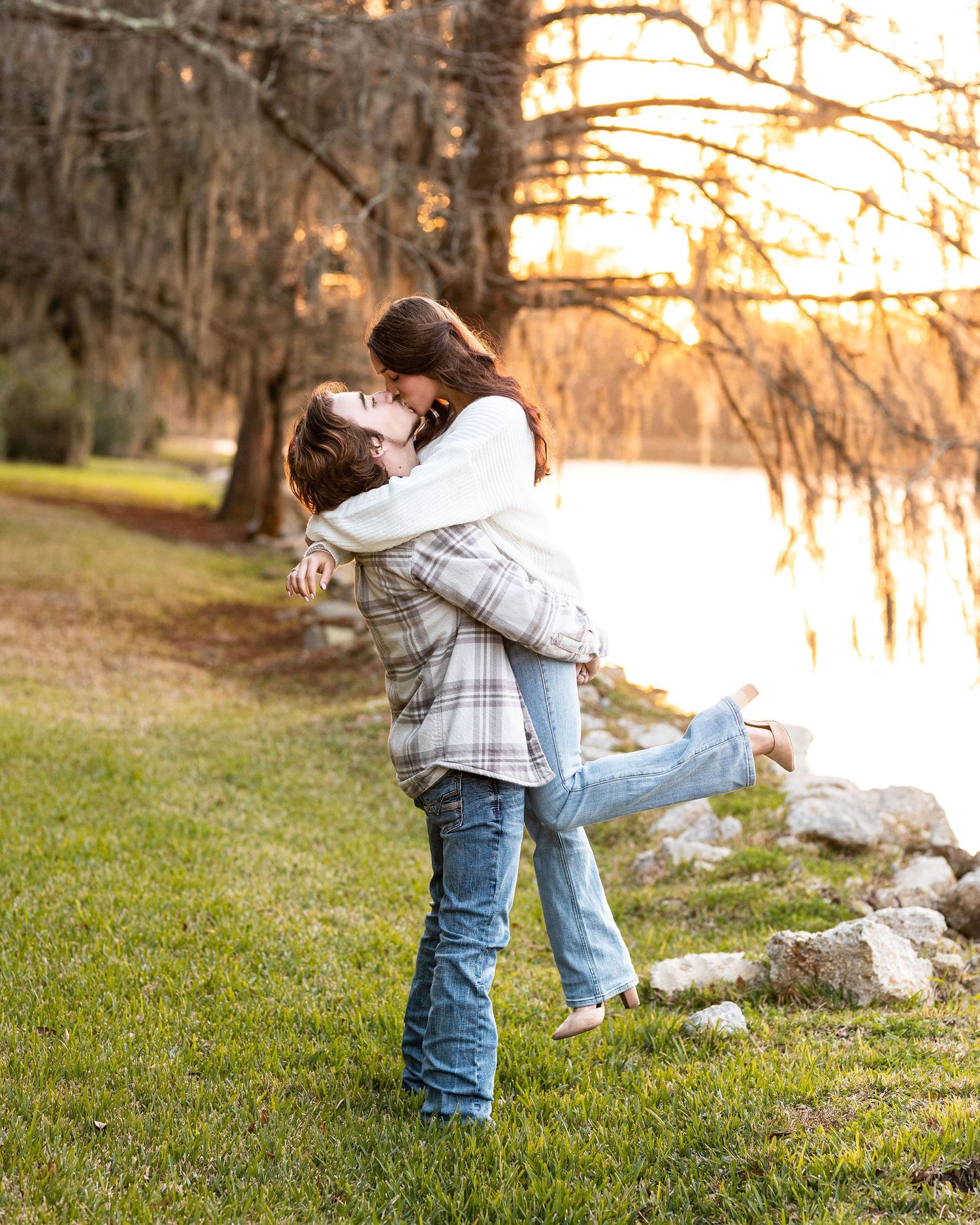 Romantic couple embracing in a park at sunset with Spanish moss hanging from trees in the background.