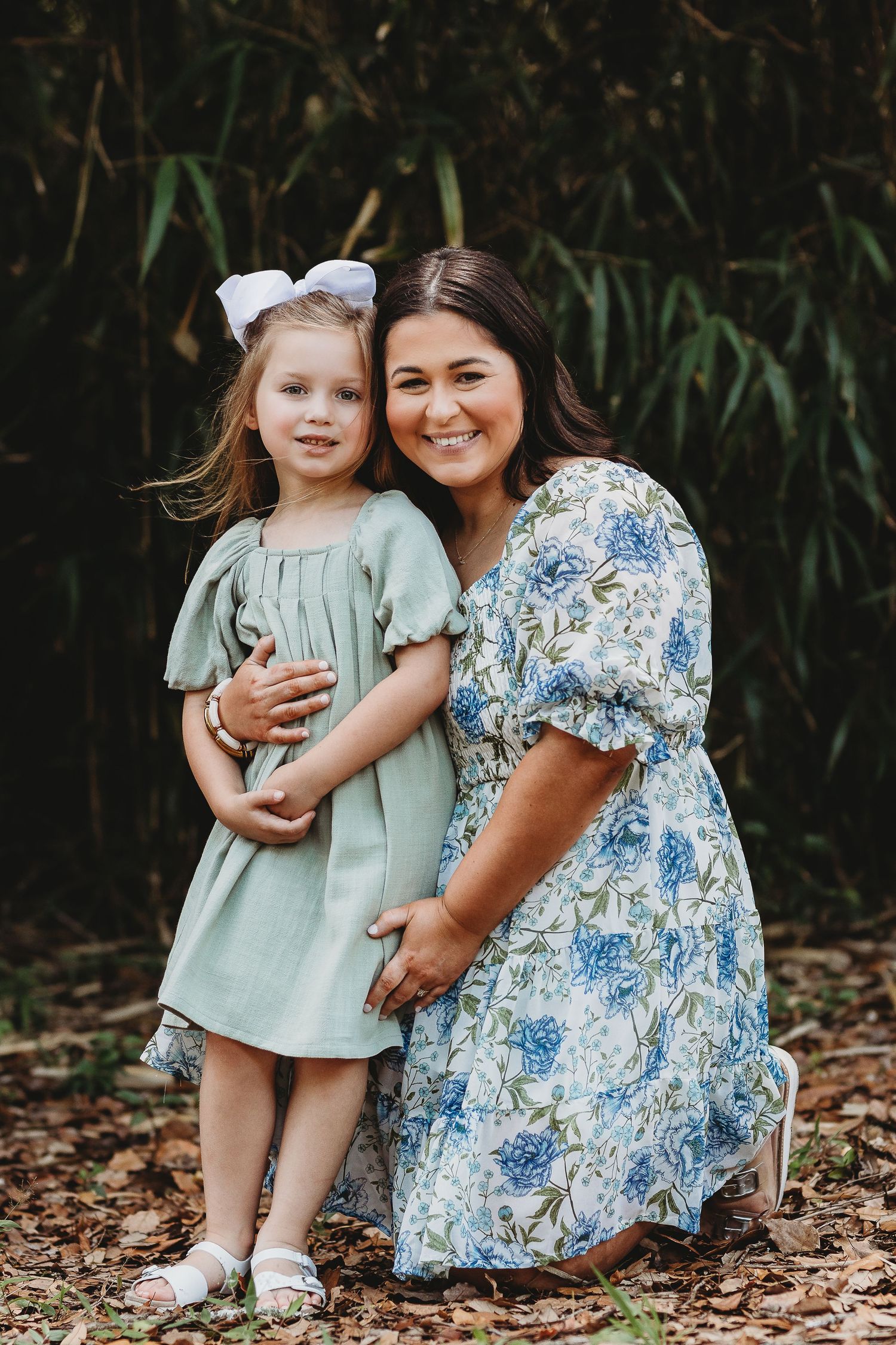 Mother and daughter in coordinating blue and mint dresses pose outdoors.
