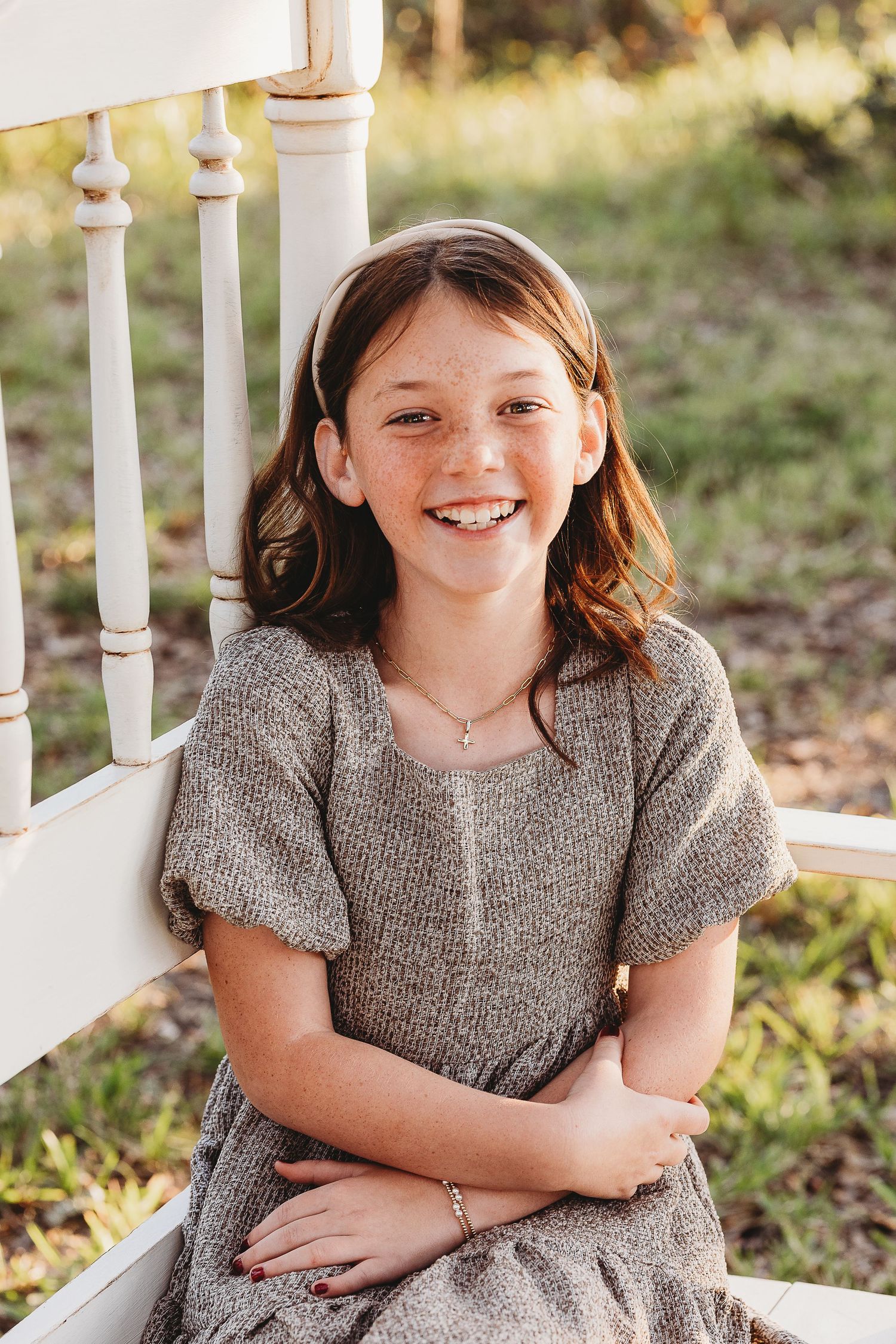 Child wearing a grey dress sitting on white porch steps in natural outdoor lighting.