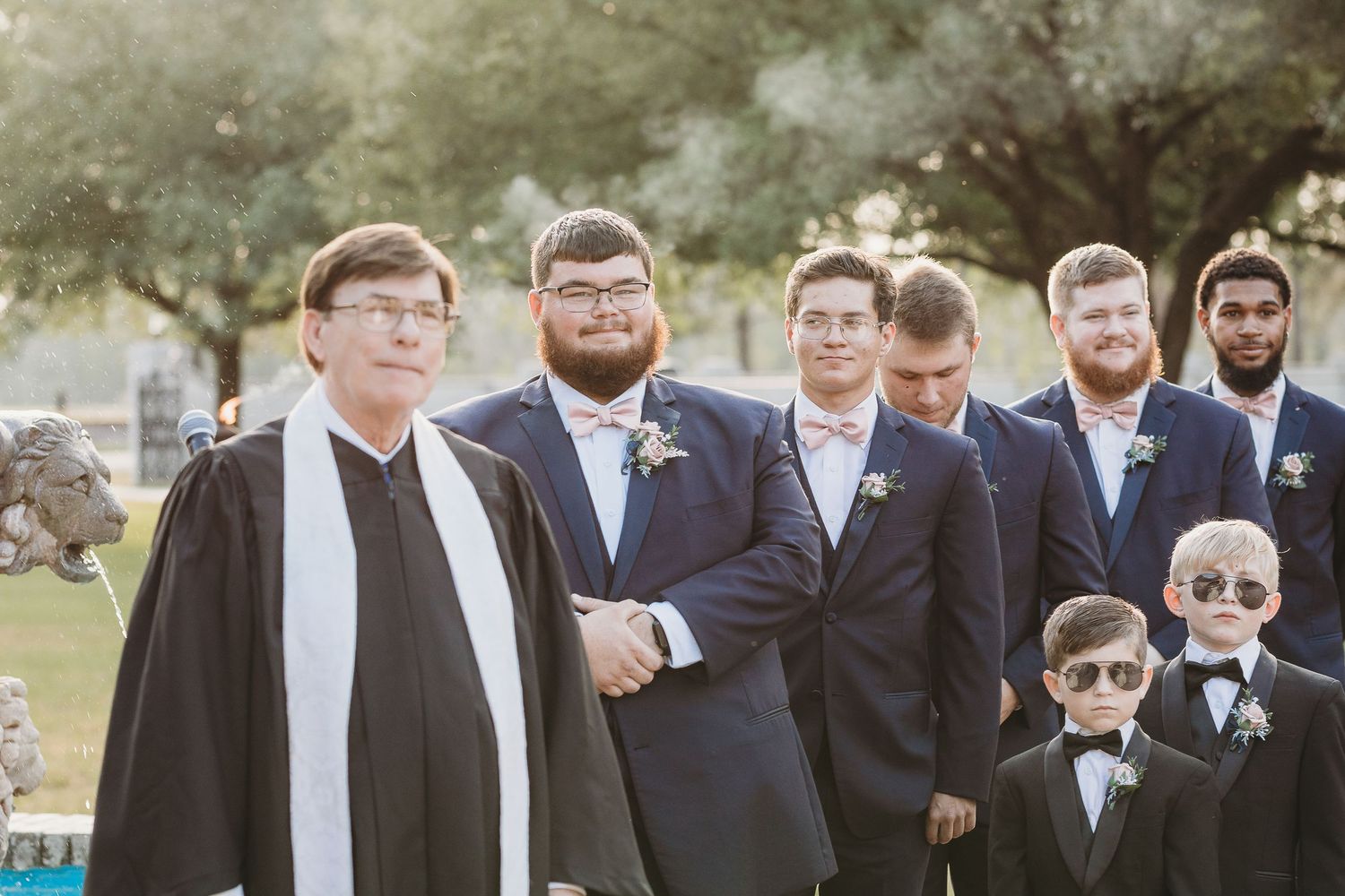 Groomsmen in formal suits pose together outdoors for wedding photos.