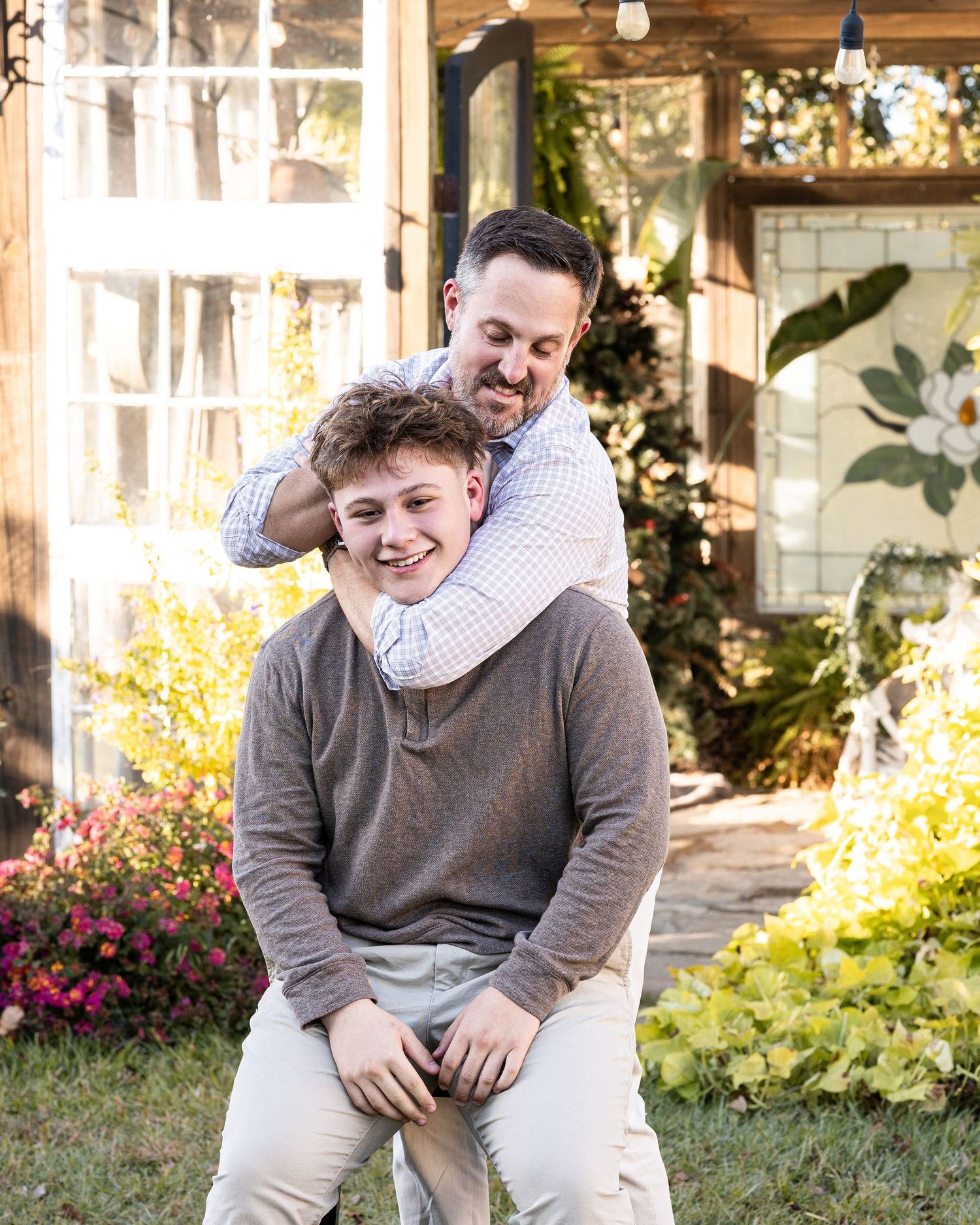 A couple sits together and laughs on wooden porch steps during a sunny autumn day.