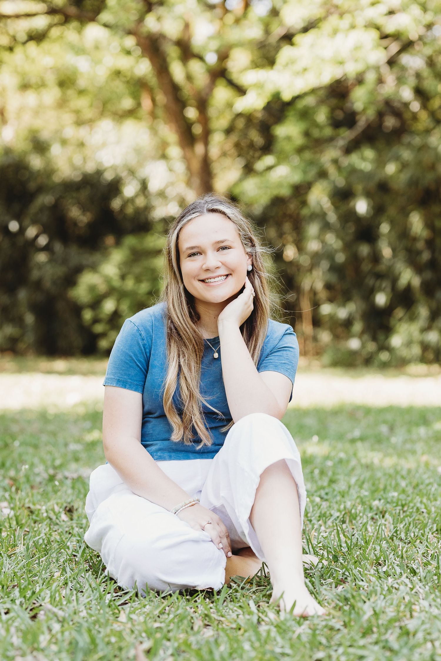 Relaxed outdoor portraits sitting on grass in casual blue top and white pants.