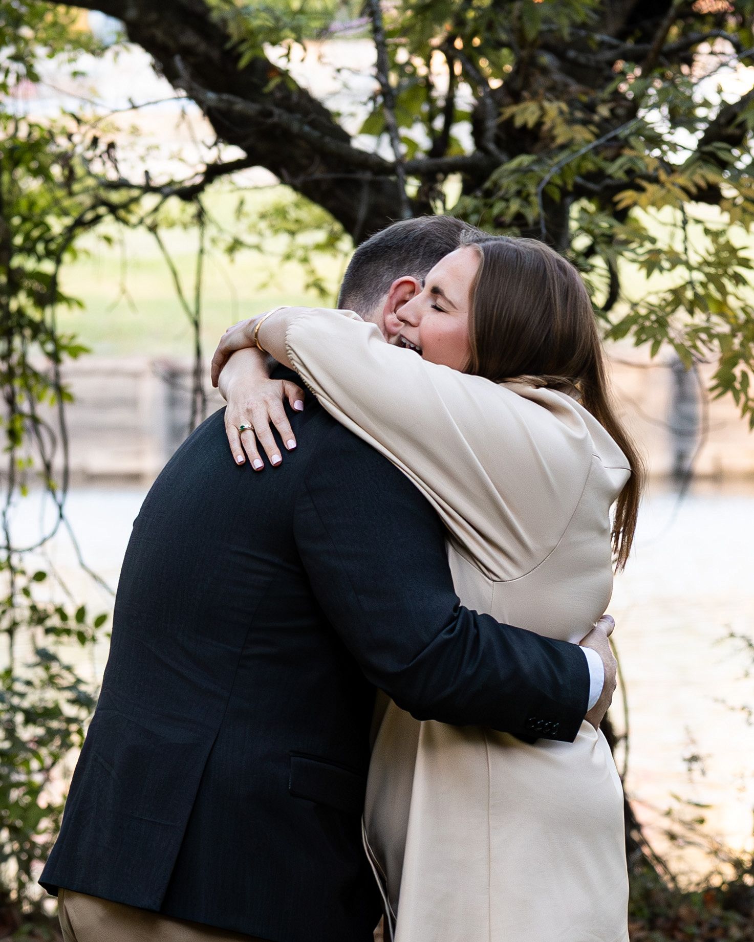 Two people share a tender embrace under a tree branch on a sunny autumn day.