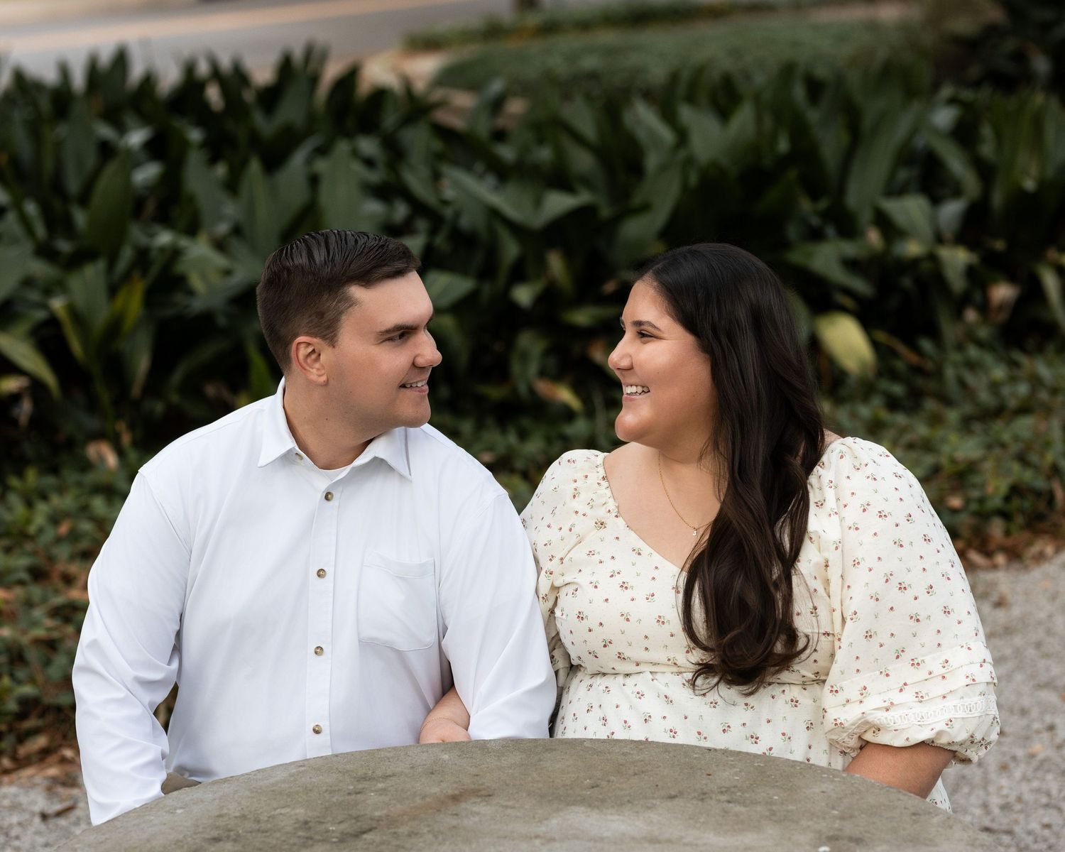 A romantic couple in white outfits sits together and shares intimate moments in a garden setting.