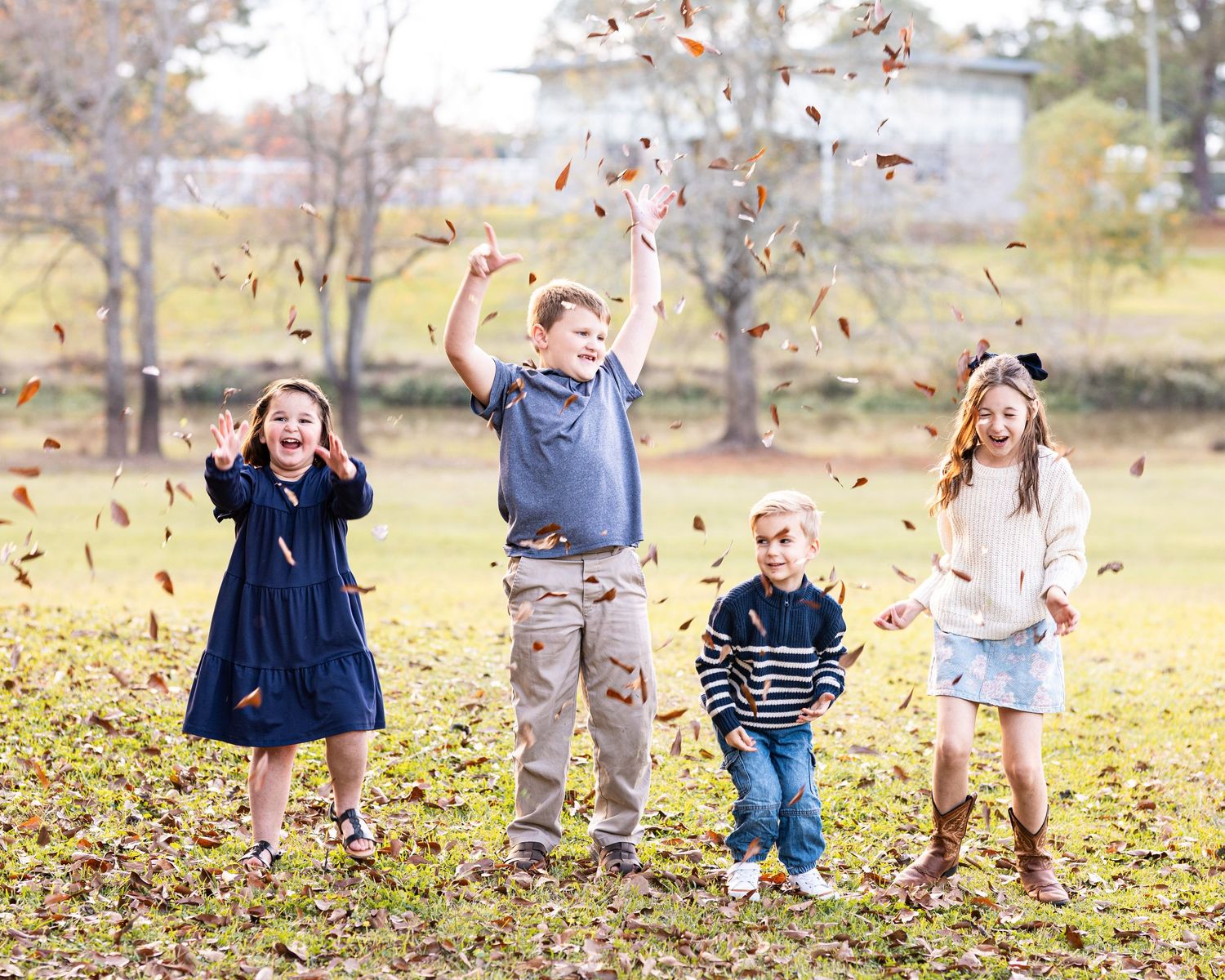 Children playing and throwing autumn leaves in a park during fall season.