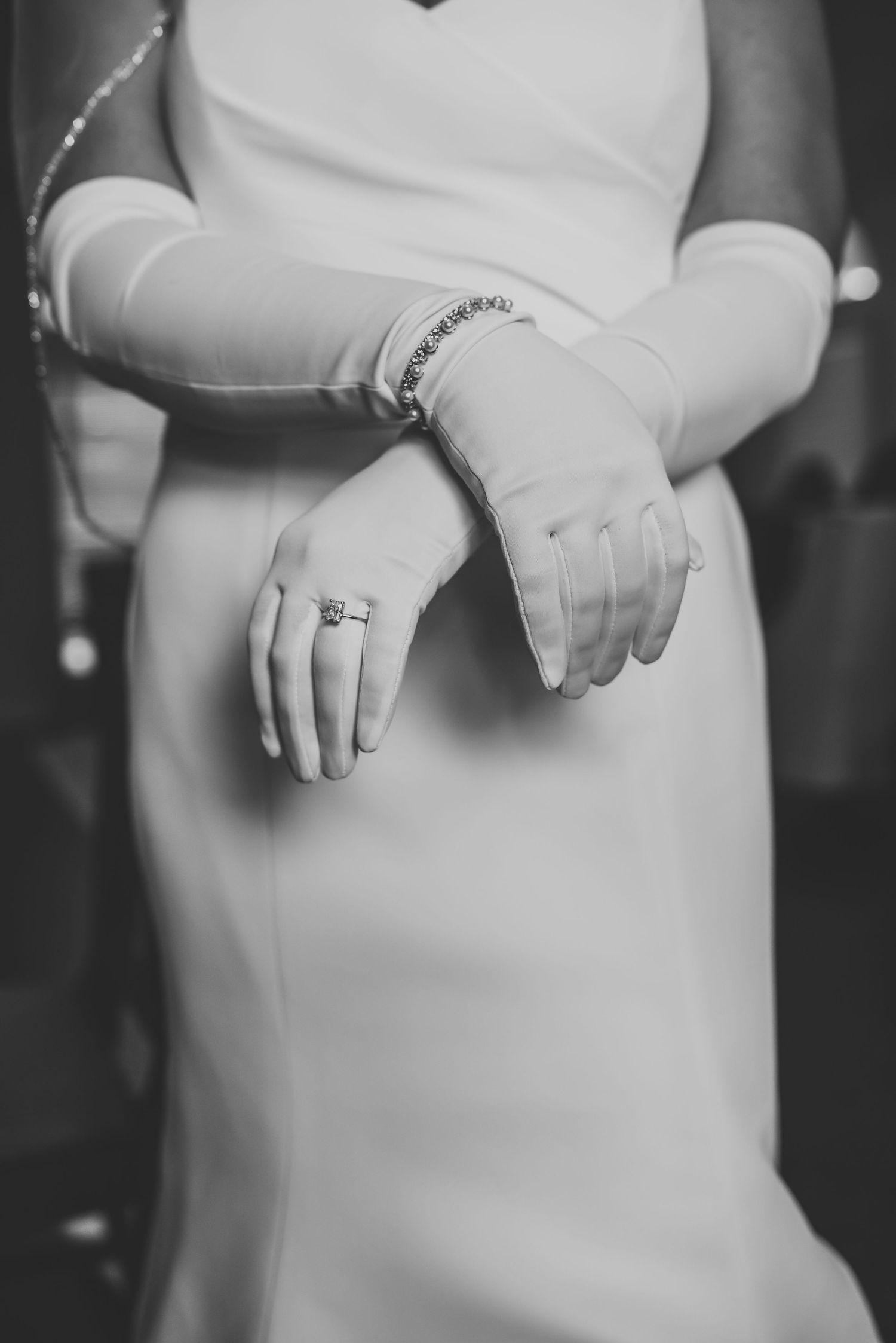 Black and white detail shot of hands wearing wedding rings against white dress.