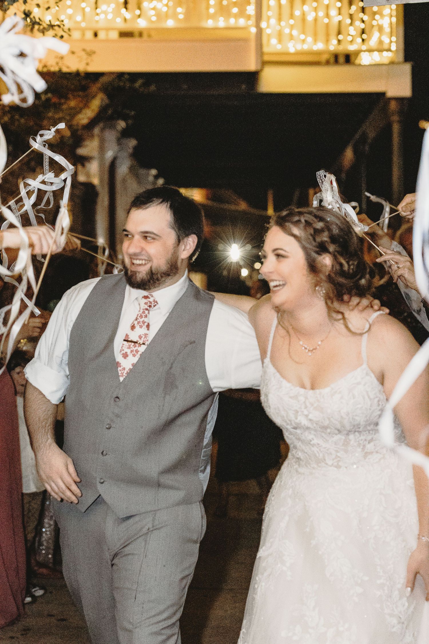 A happy couple exits their wedding reception under a tunnel of waving ribbon wands.