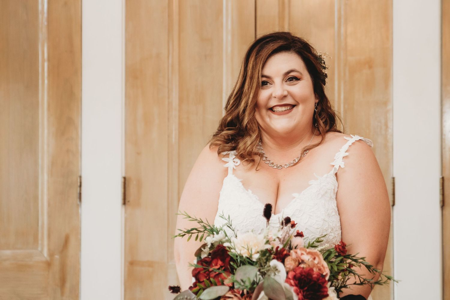 A bride holds a stunning bouquet featuring red and white flowers with greenery.