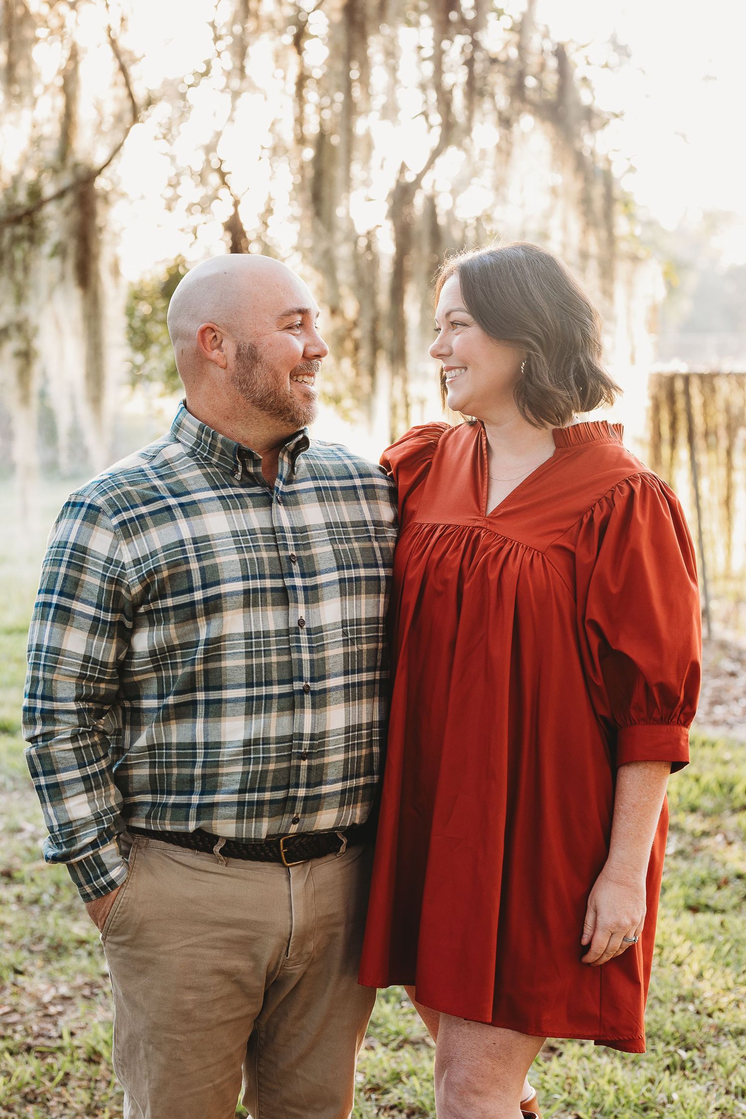 Couple in plaid shirt and red dress sharing tender moments in a sunlit wooded setting.