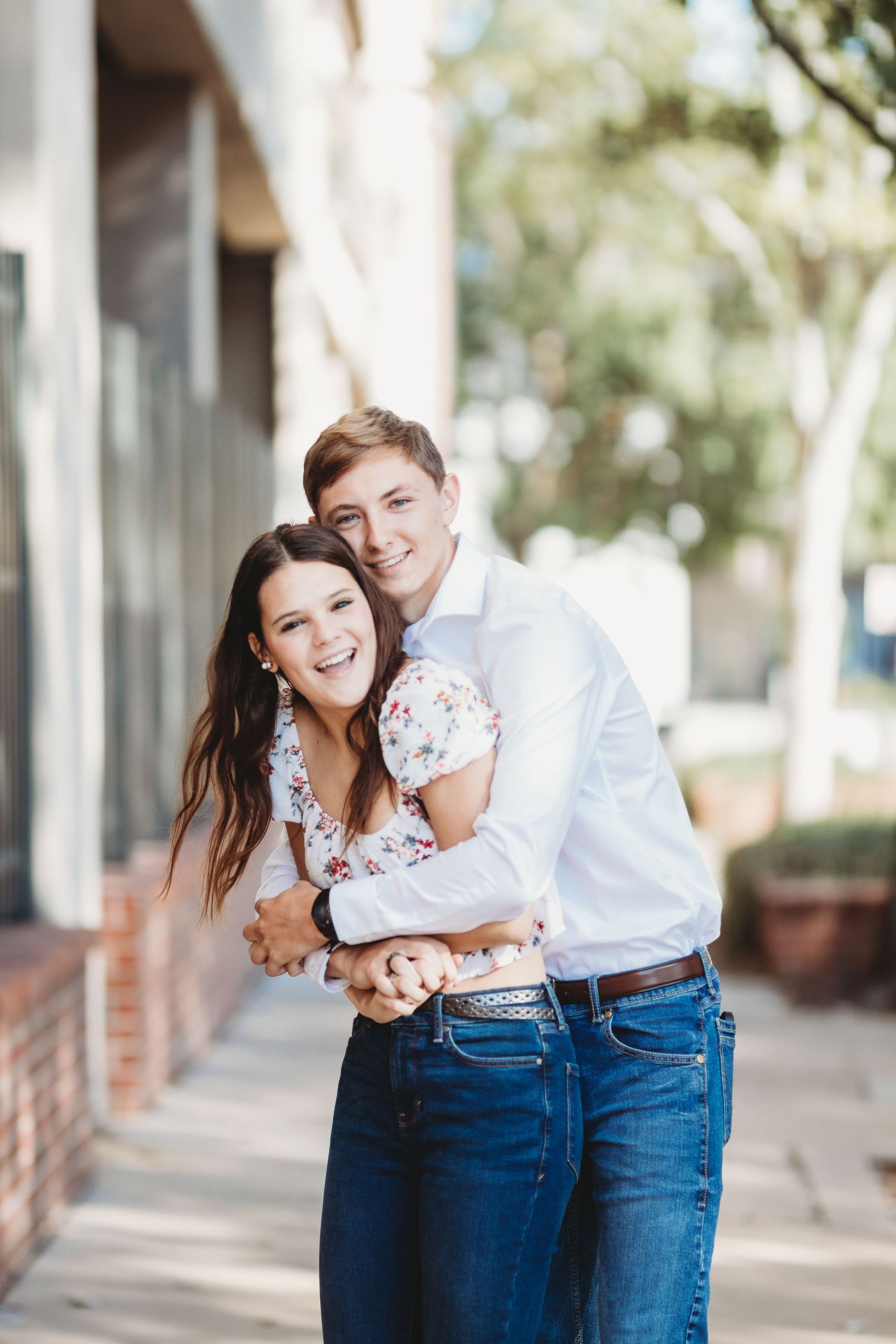 A couple in coordinated outfits laughs together under a covered walkway with columns.