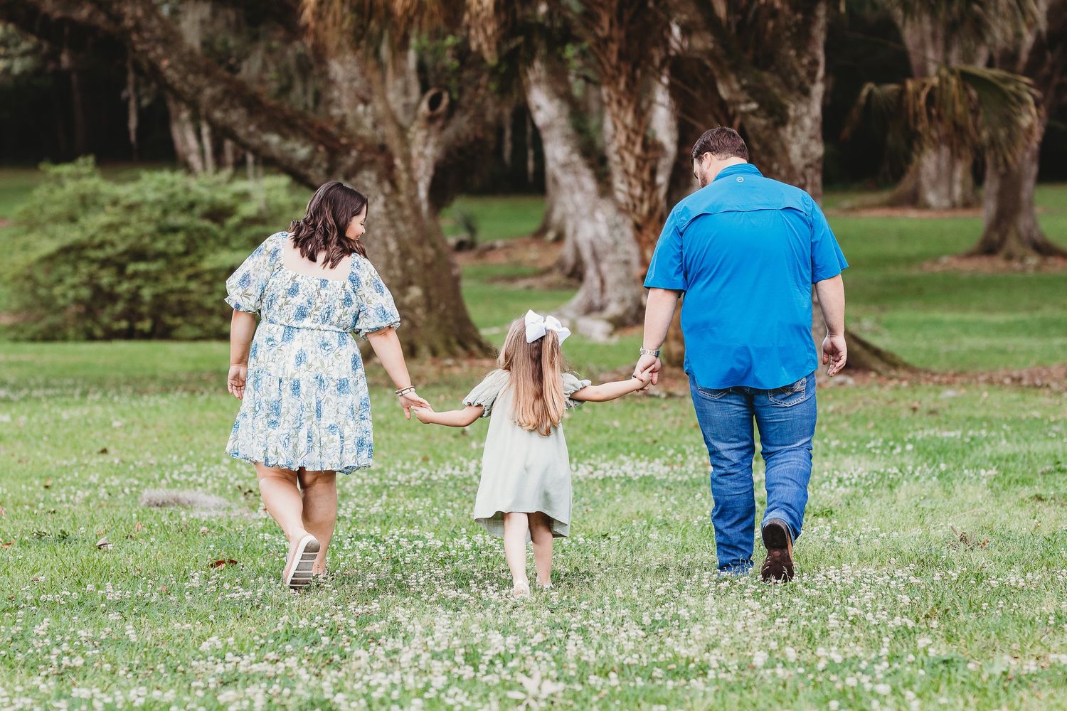 Family walking together on grass path through scenic wooded area.