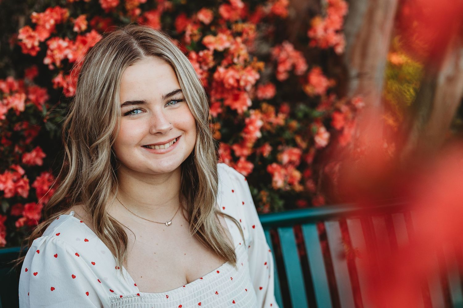 Outdoor portrait with vibrant red flowers in background.