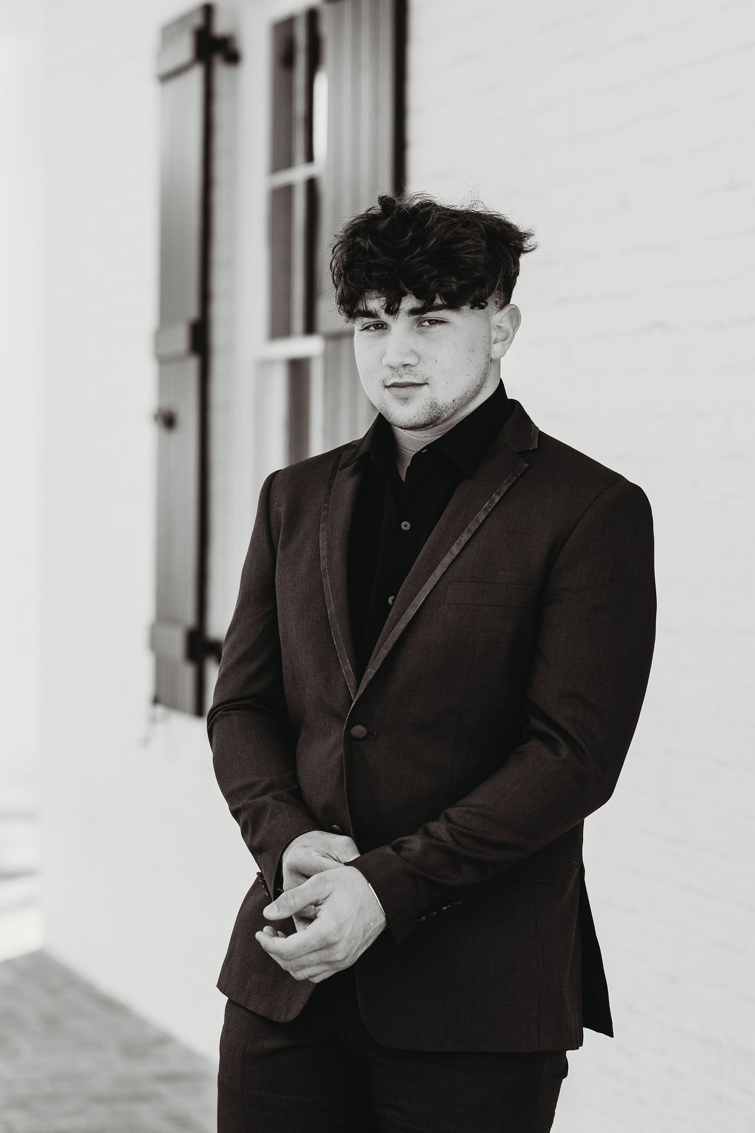 Black and white portrait of someone in a dark suit and black shirt.
