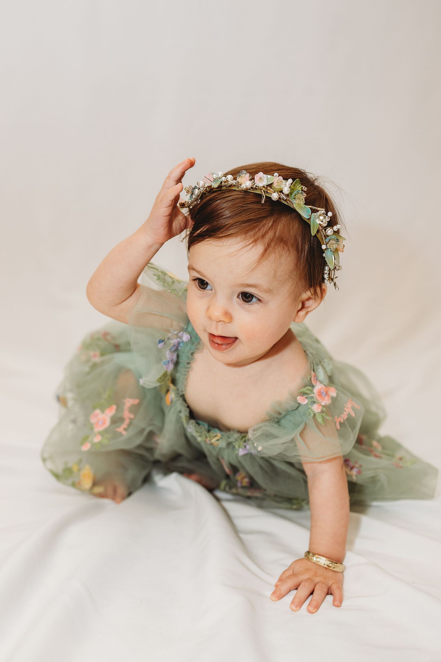 Baby in mint green floral dress crawling on white background.