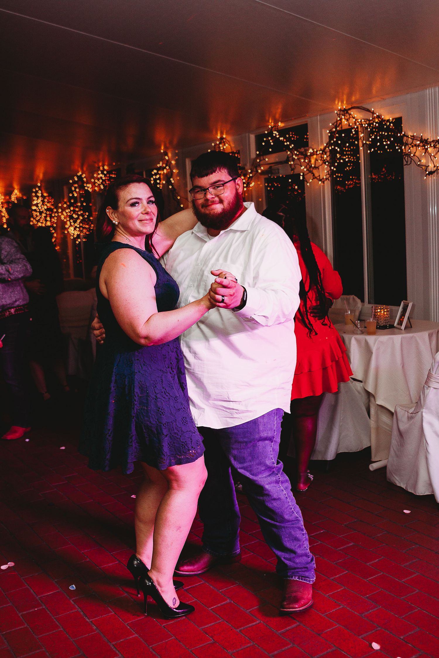 Couples slow dancing at a wedding reception with string lights and decorations creating a romantic ambiance.