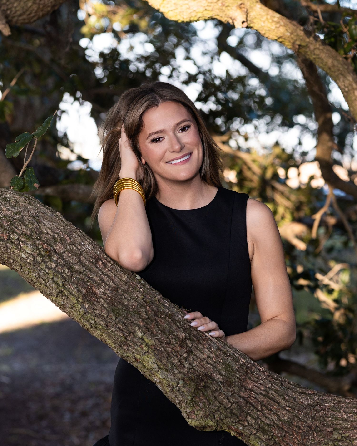 Portrait of someone in a black sleeveless top posing by a tree branch with soft bokeh lighting in the background.