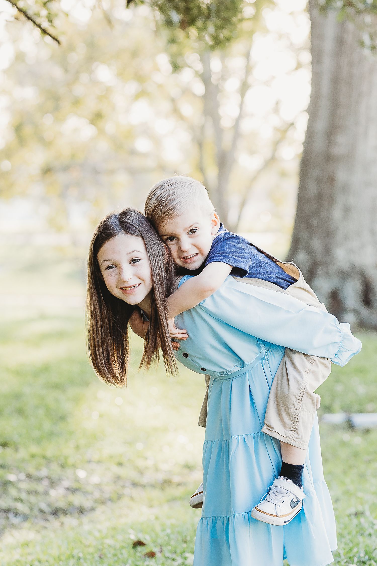 Children playing and hugging outdoors among trees in natural lighting.