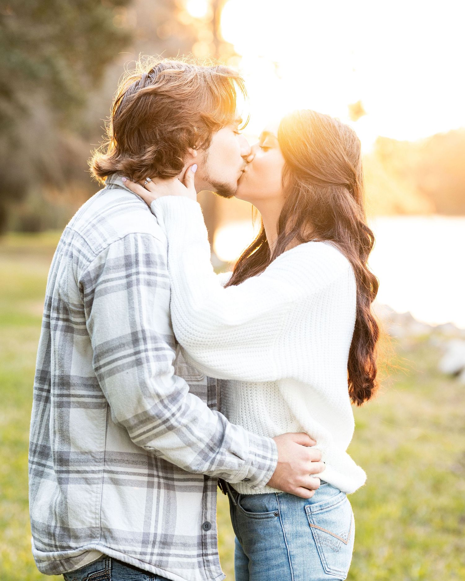Couple embraces lovingly in a park during golden hour sunset while wearing casual autumn attire.