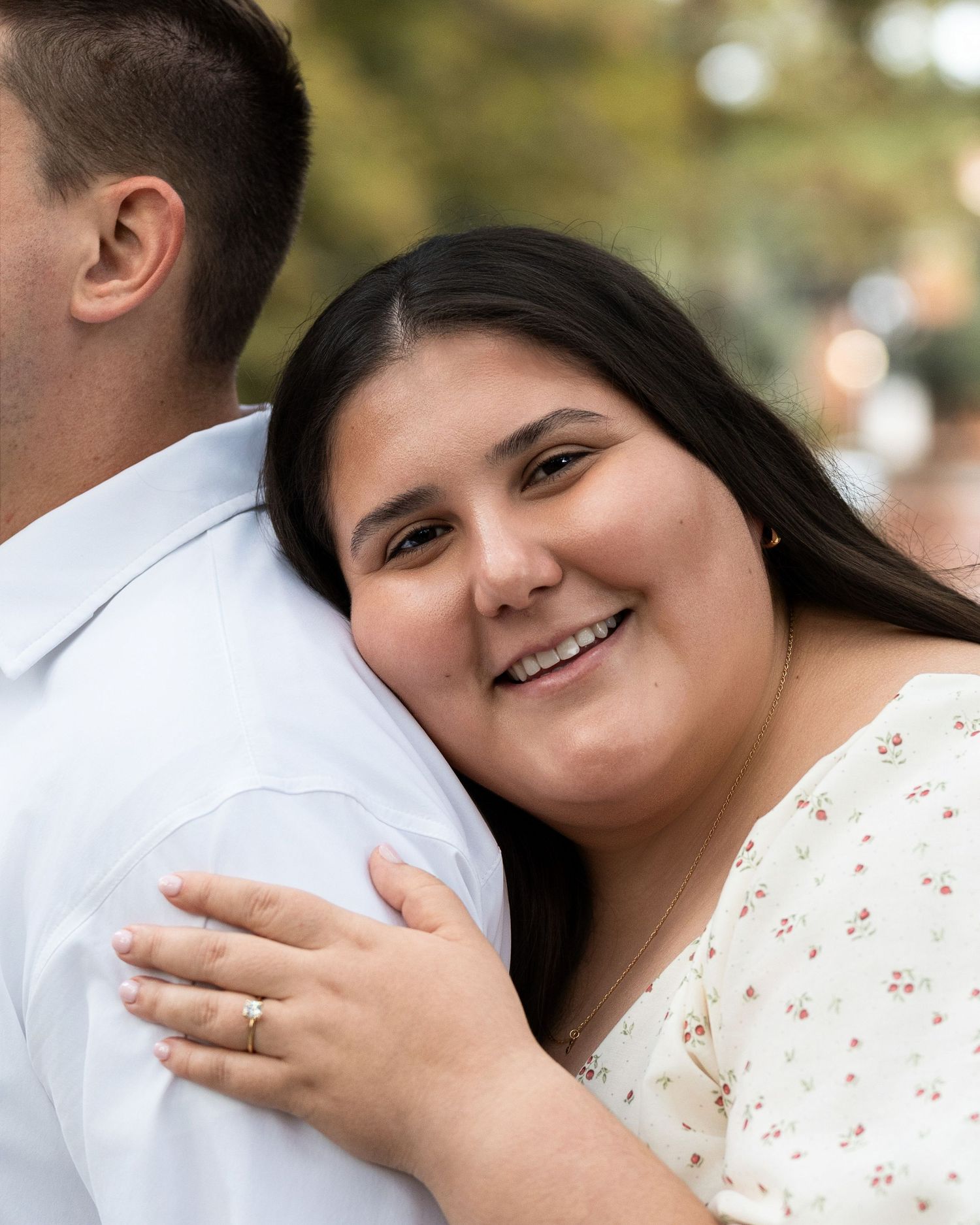 A couple embraces and smiles during an outdoor photo session wearing white and floral outfits.