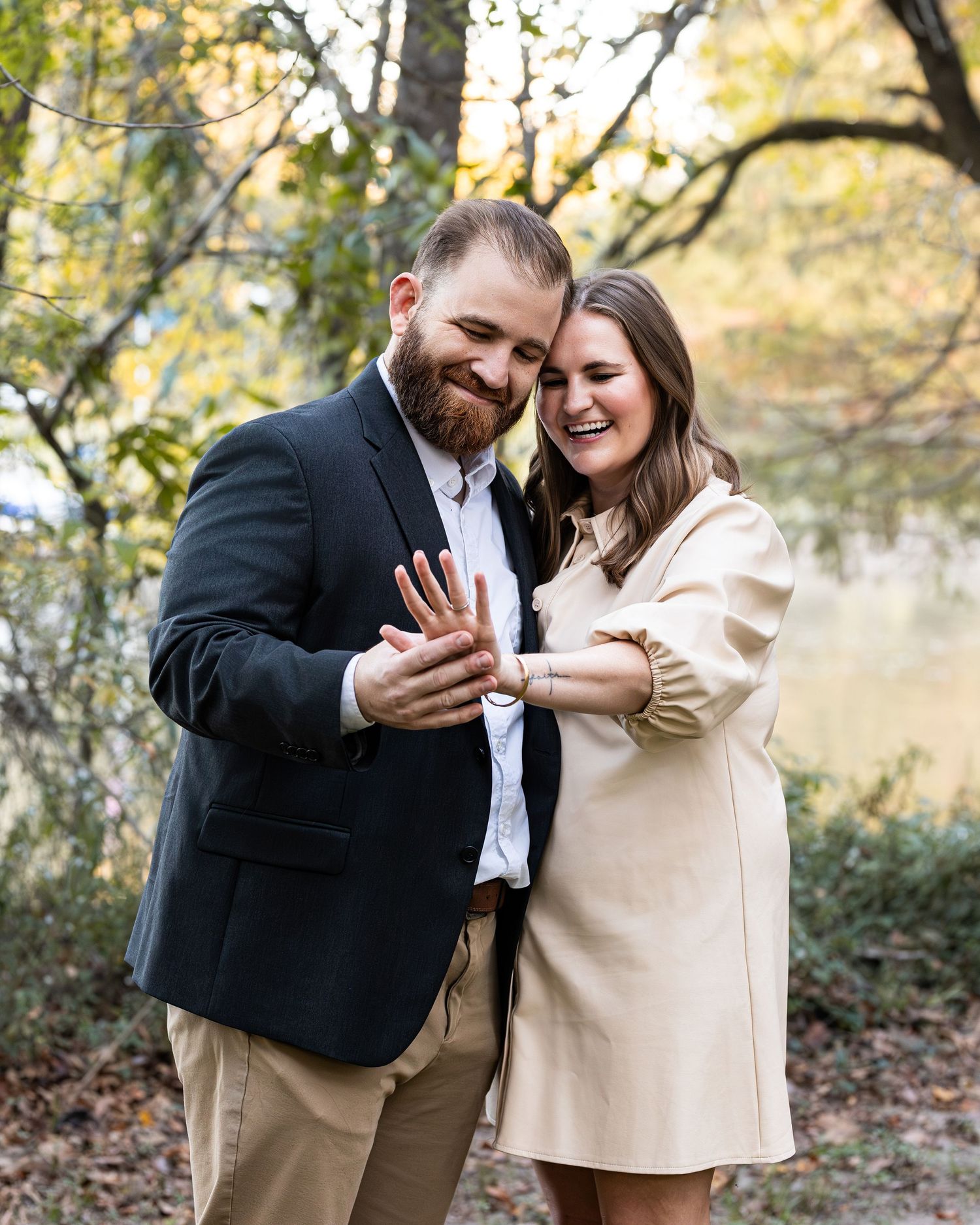 A couple laughs together during a romantic autumn engagement session in a wooded setting.