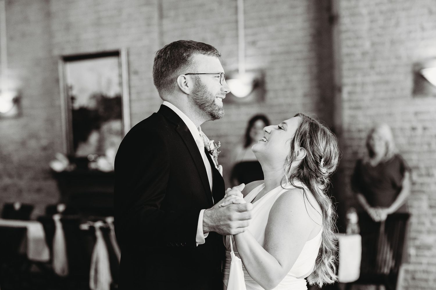 Black and white wedding photos showing dancing and celebration in a rustic brick-walled venue.