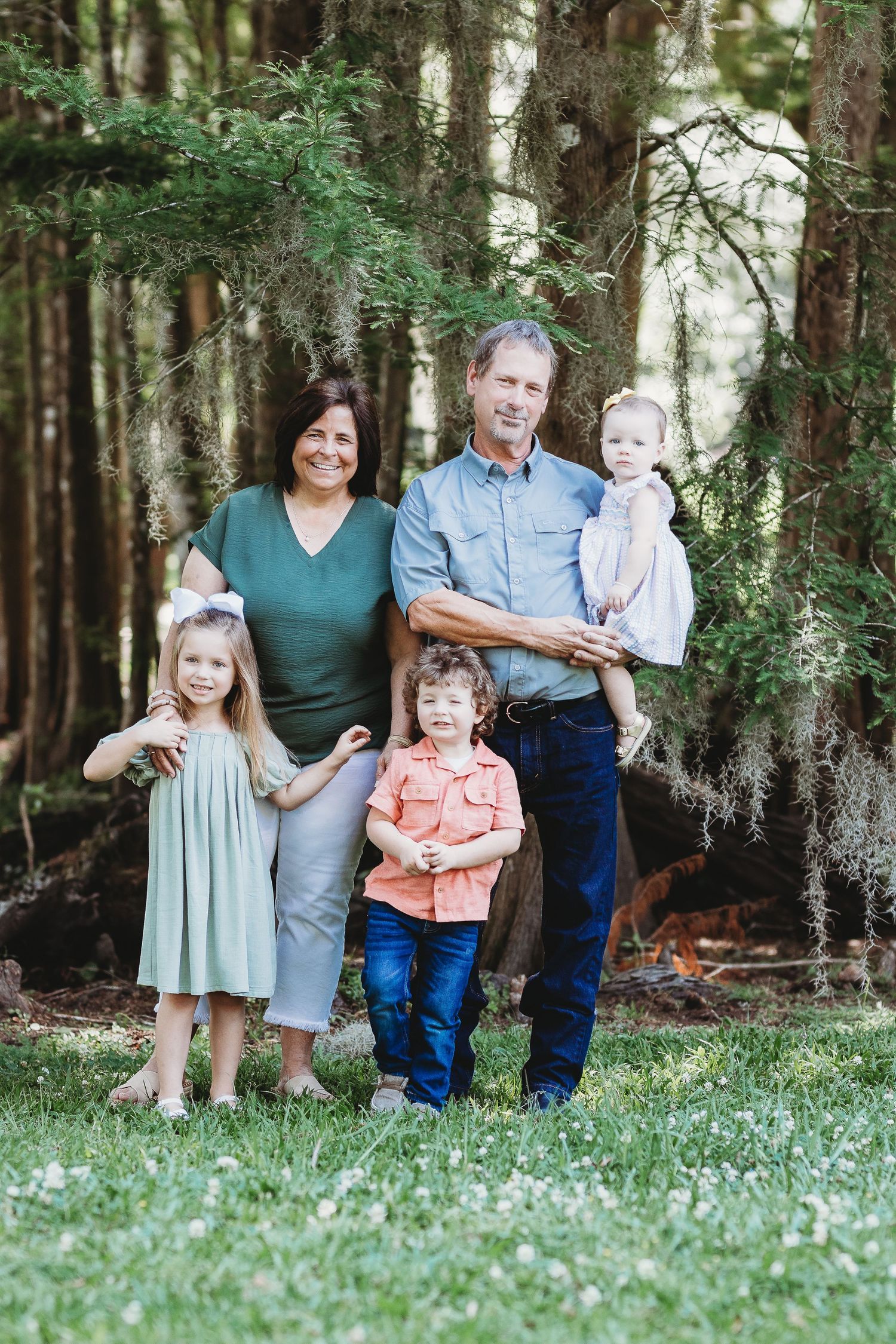 Family group portrait on grassy lawn surrounded by tall pine trees.