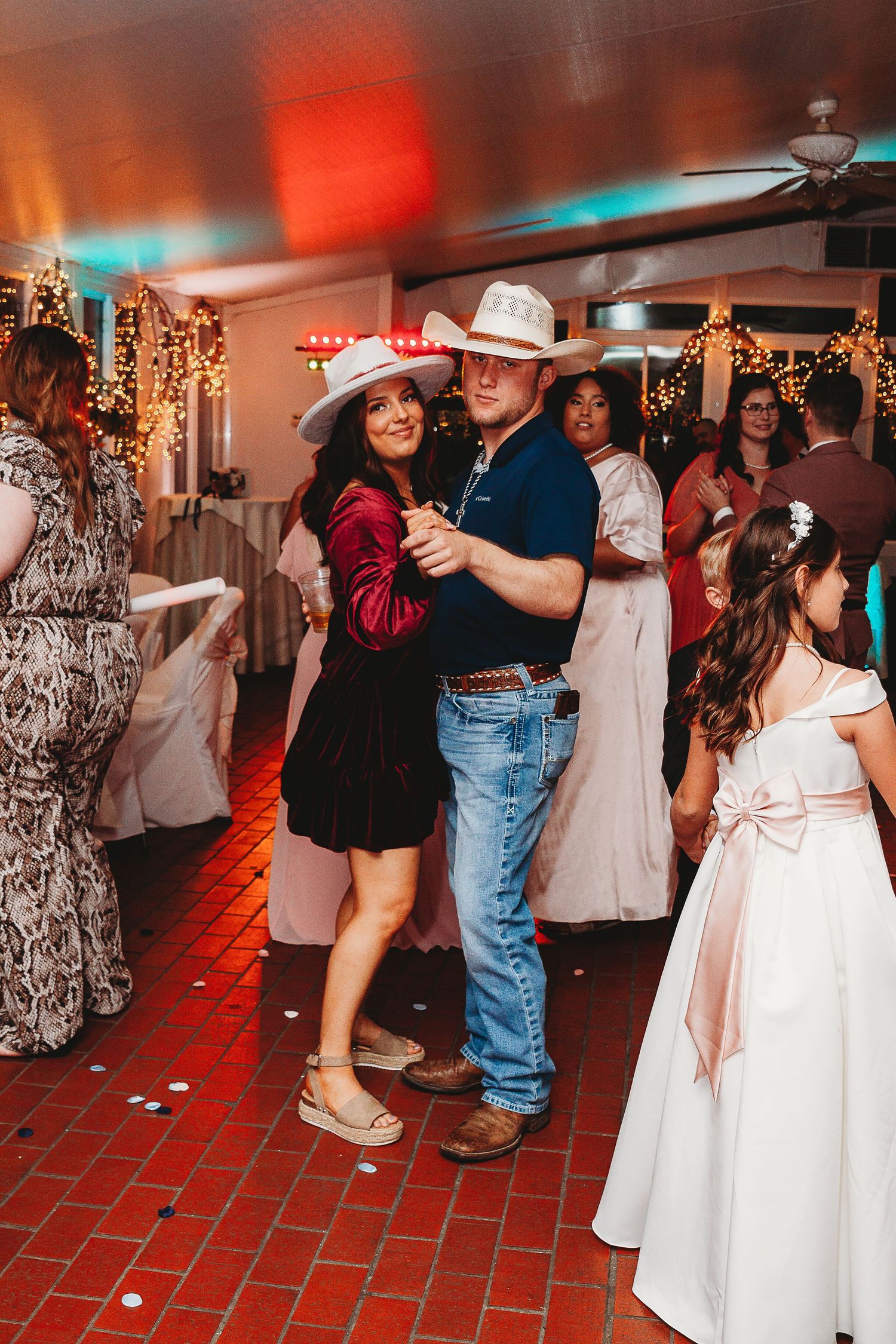 Wedding party dancing on a red brick floor with colorful lighting and decorations.