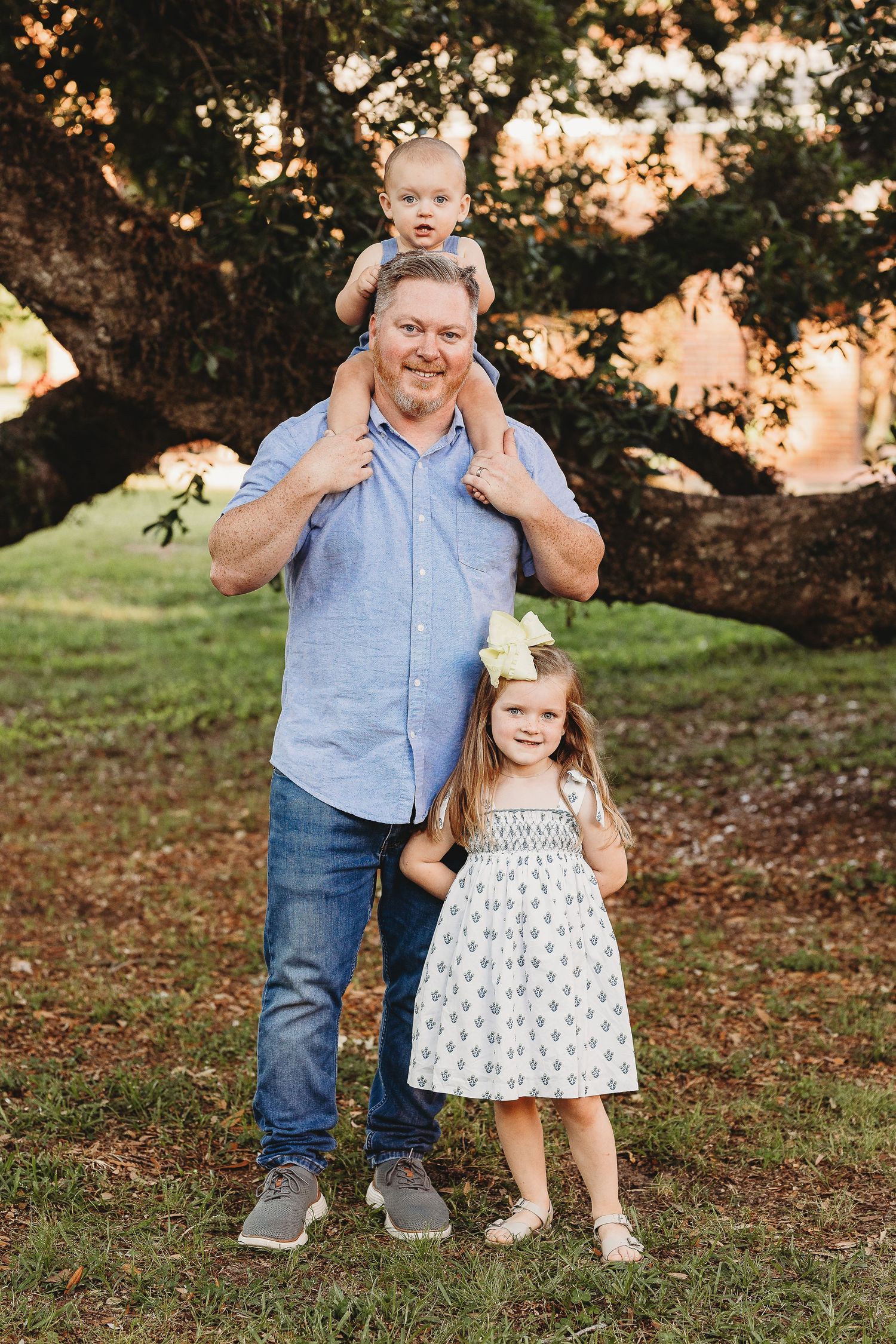 Candid family portrait under trees with warm sunset lighting and natural expressions.