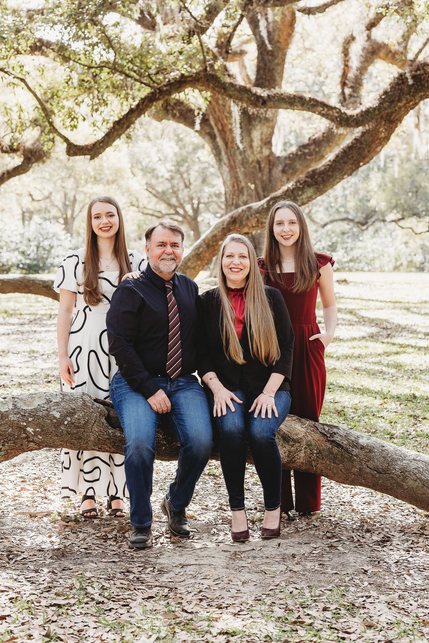A casual family photo session under a sprawling oak tree with everyone sitting on exposed roots.