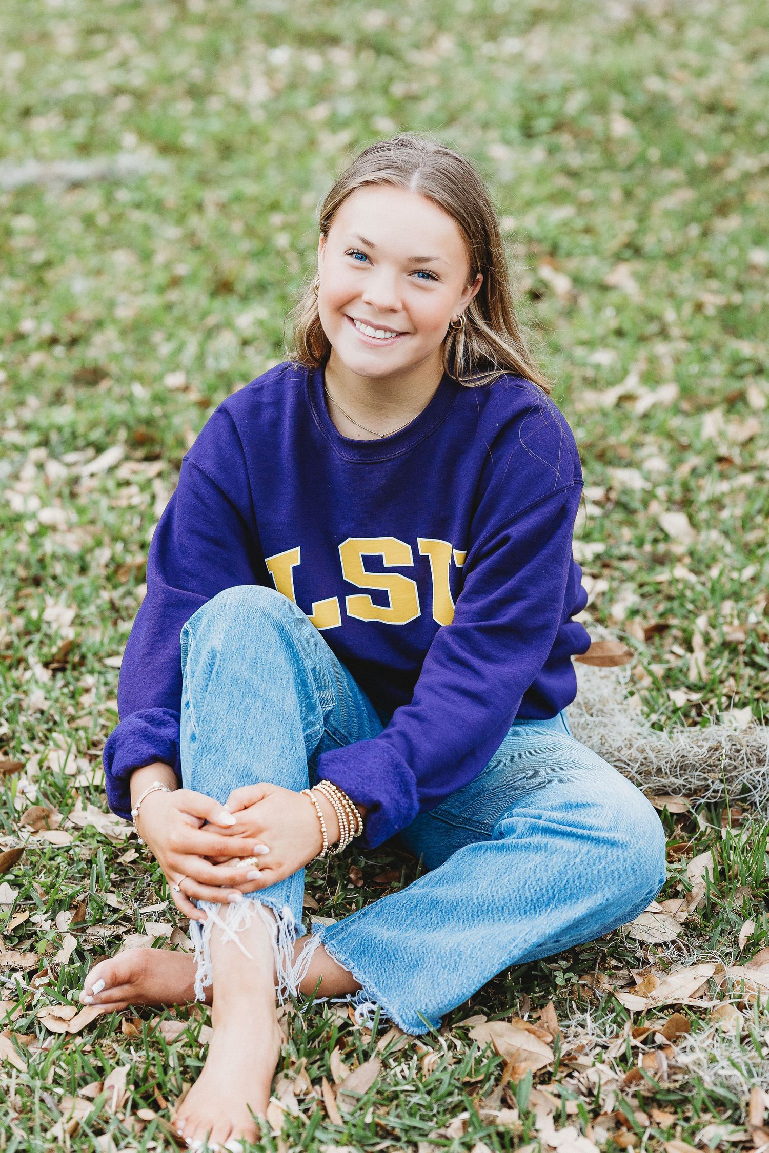 Person wearing LSU sweatshirt sits casually on grass during outdoor photoshoot.
