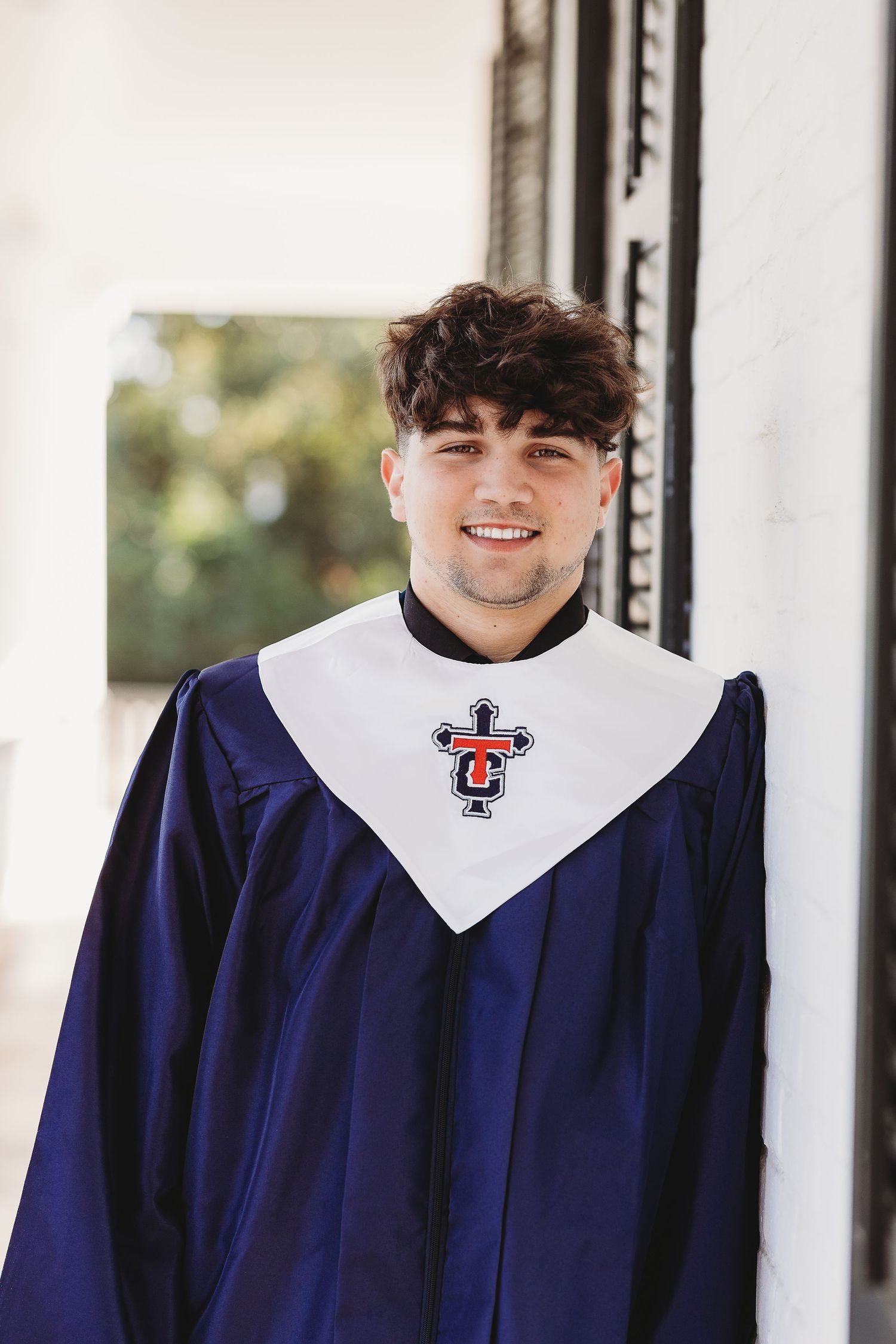 Graduate wearing navy blue graduation gown with white collar and university emblem.