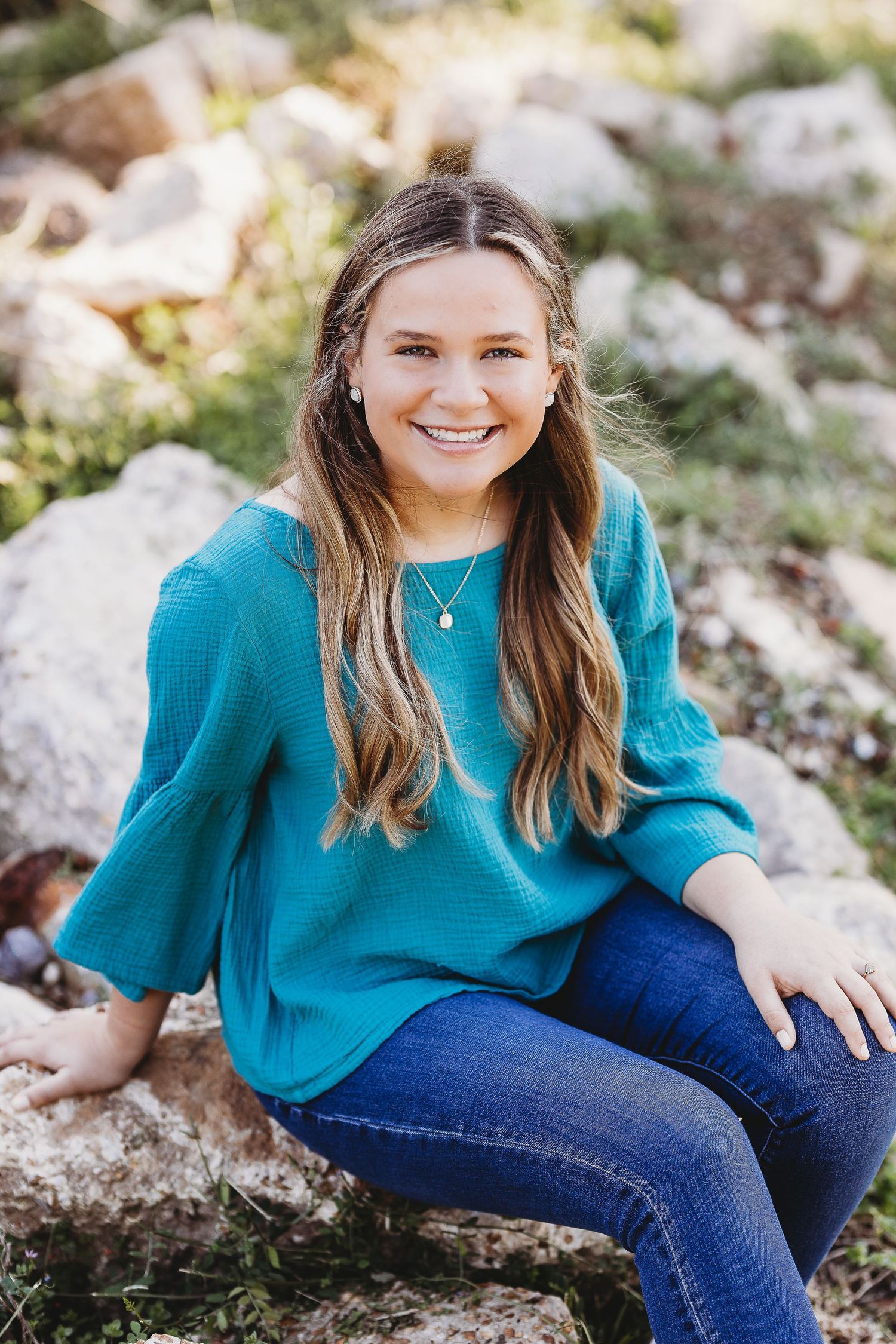 Portrait session featuring person in teal sweater and jeans sitting on rocky terrain.
