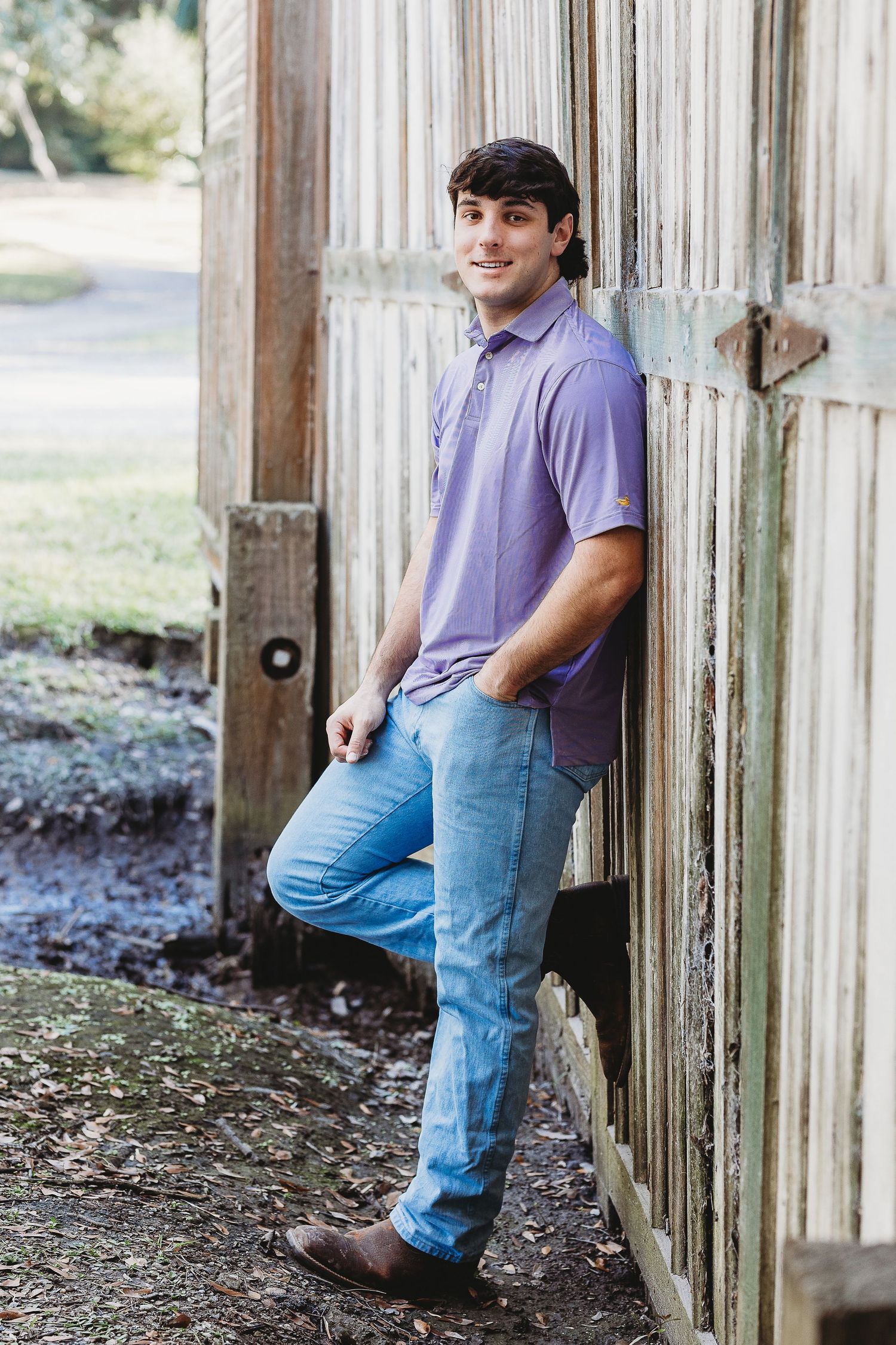 Casual portraits against rustic wooden wall in purple polo and jeans.
